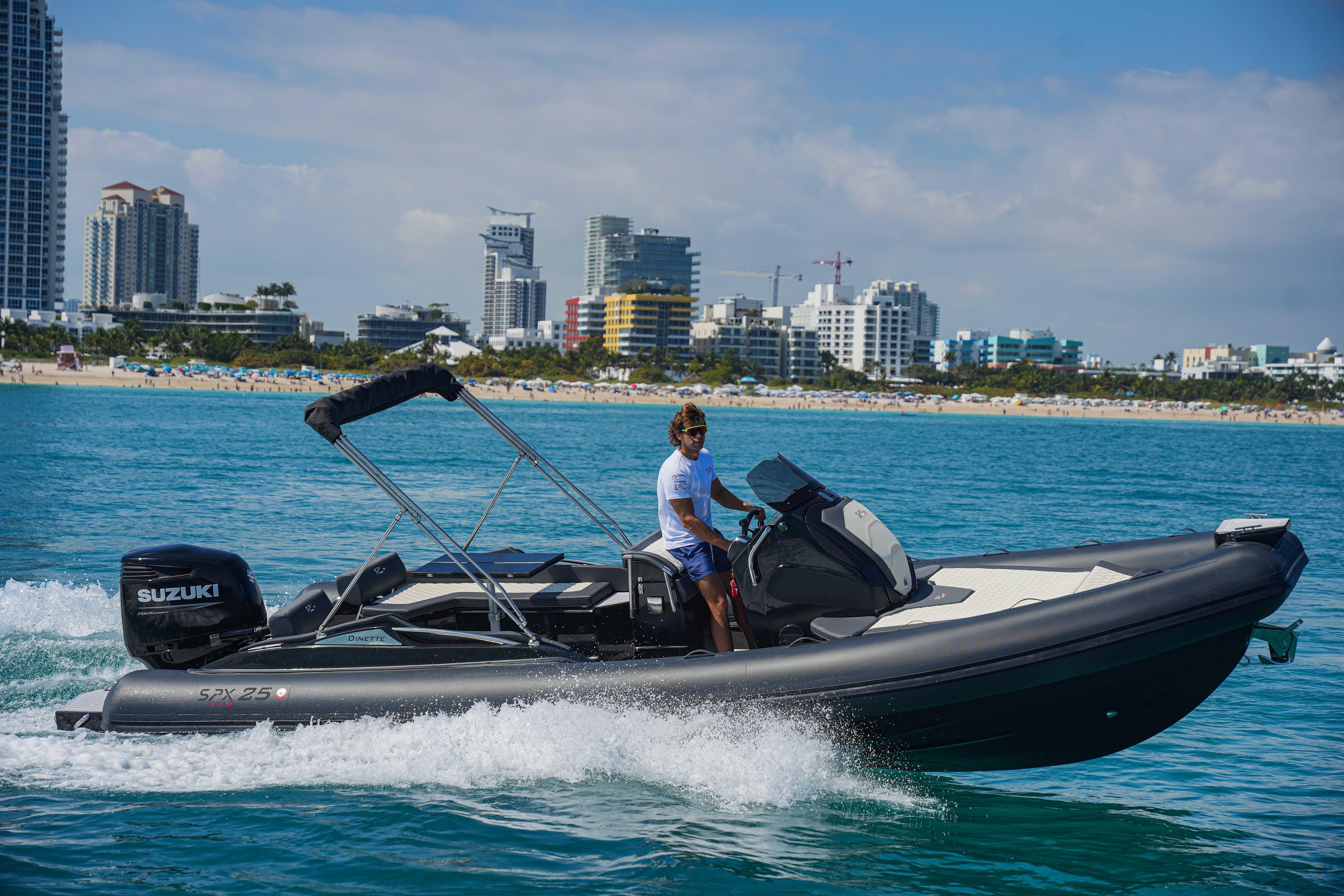 2023 SPX RIB 25 Dinette boat cruising near a city shoreline.