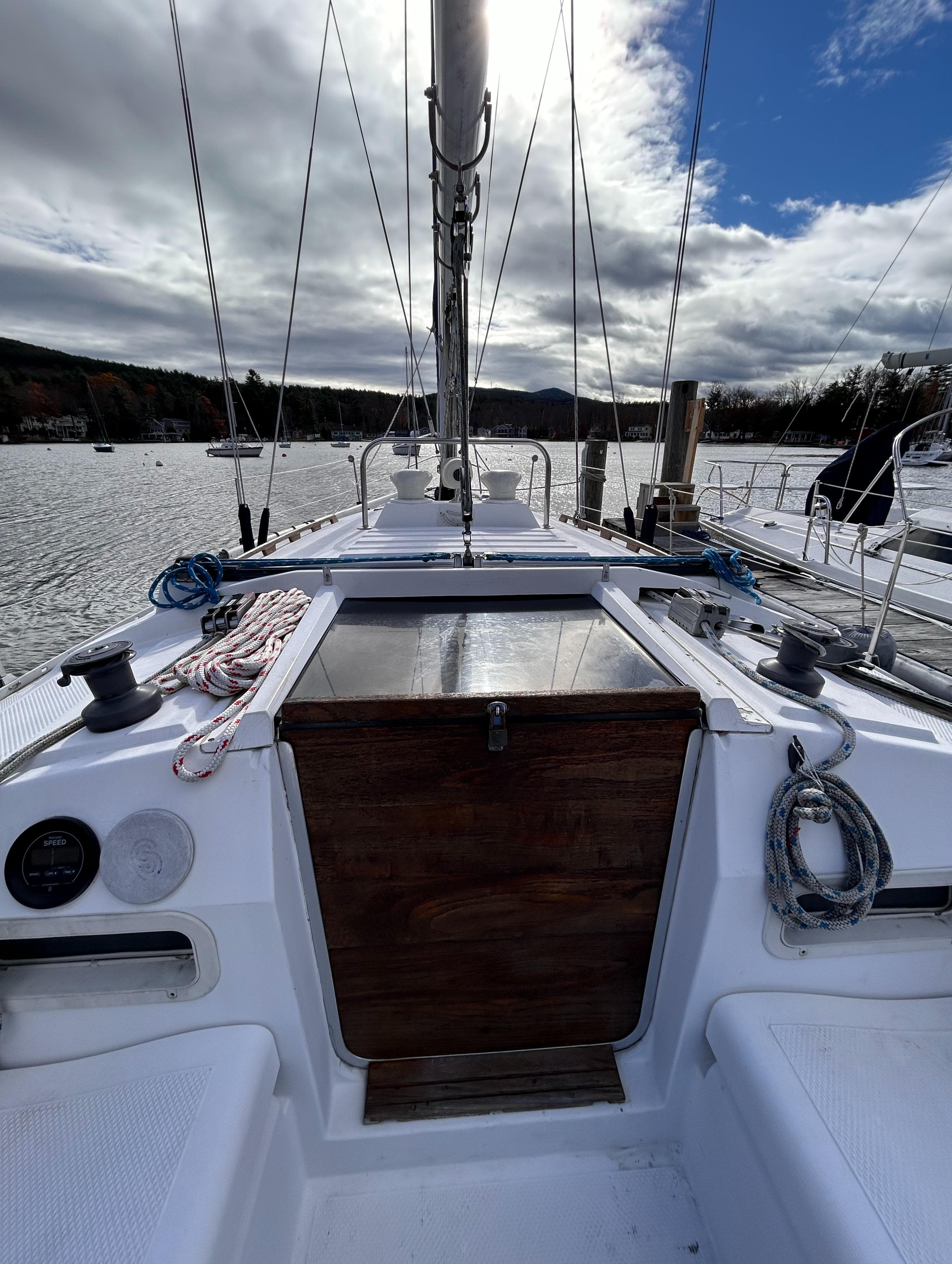 1983 Hunter 34 sailboat cockpit with ropes and winches, moored on a calm lake under cloudy skies.