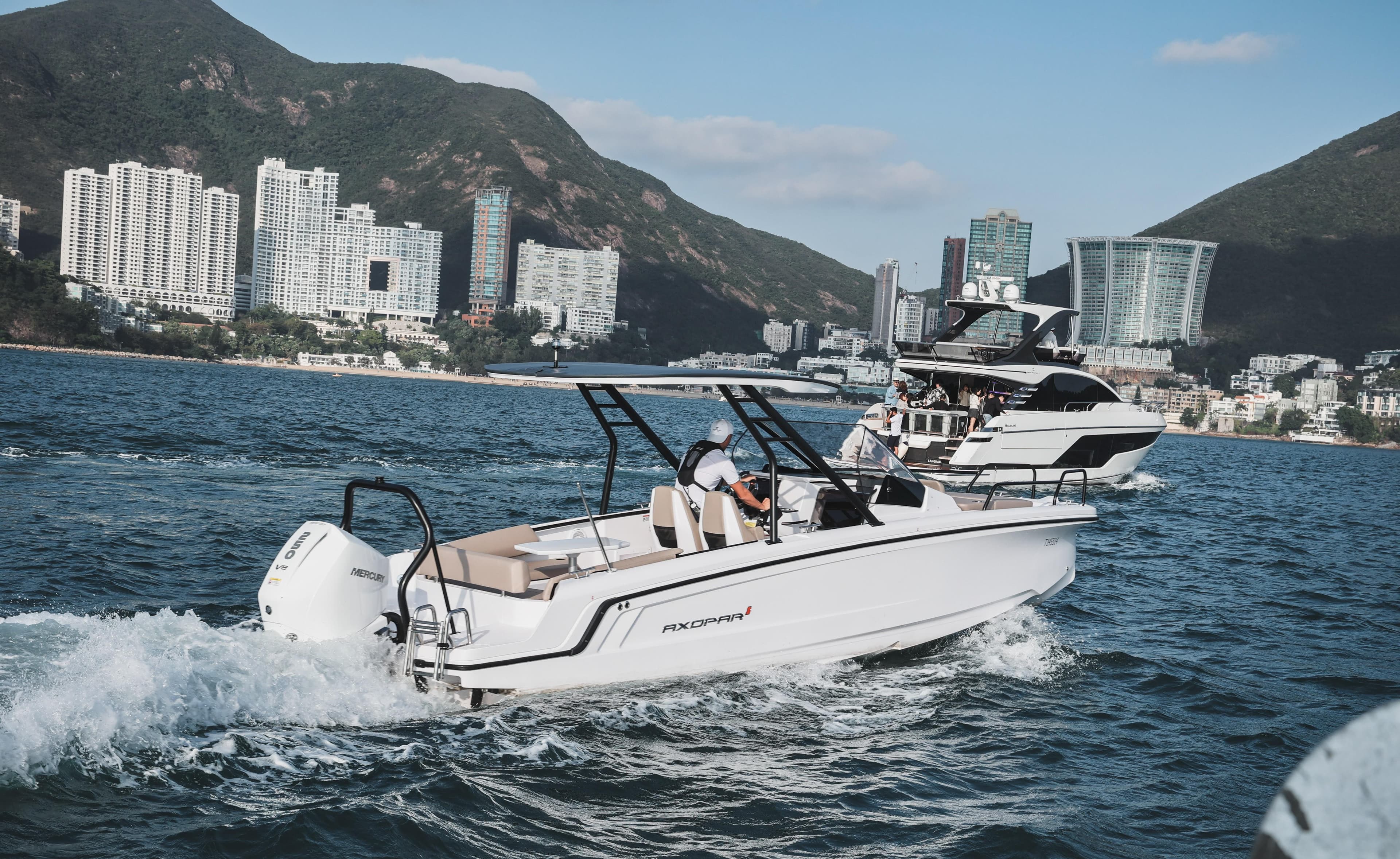 2025 Axopar 25 Cross Top boat cruising near city skyline and mountains.