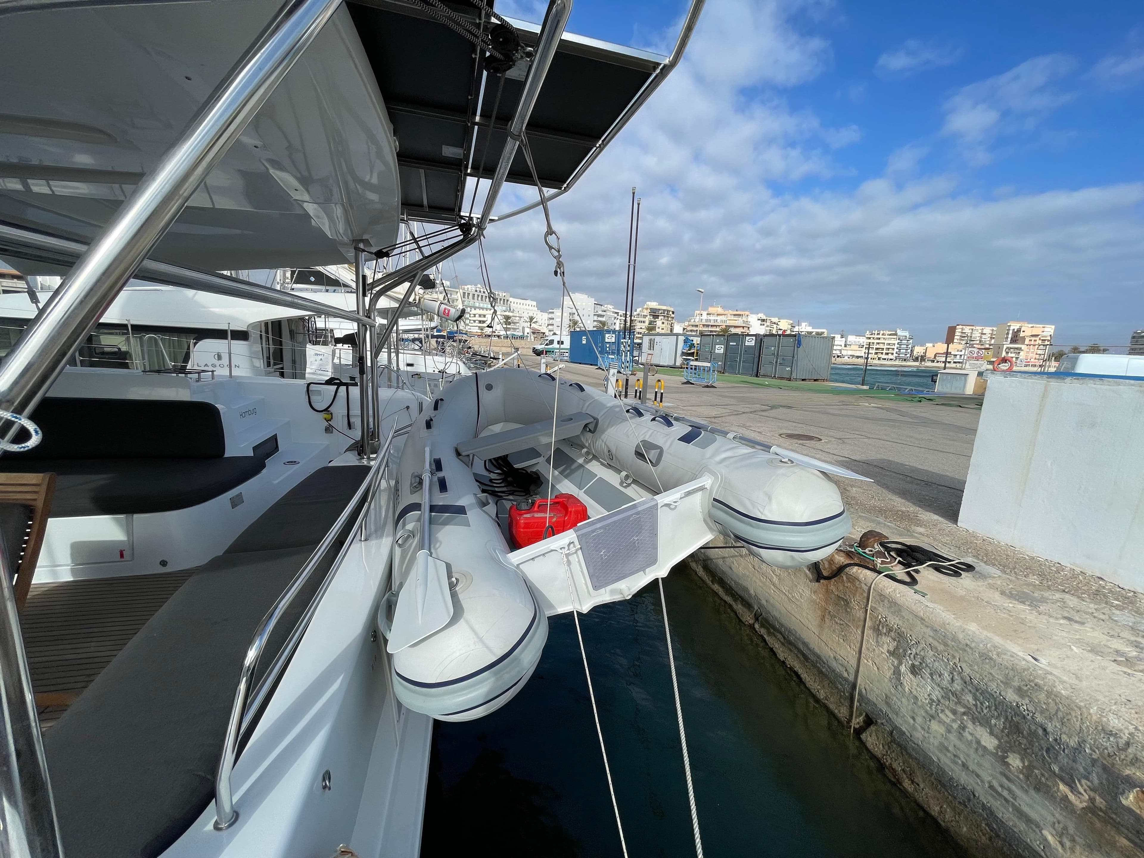 2022 Lagoon 46 yacht docked with inflatable dinghy, clear sky, and urban backdrop.