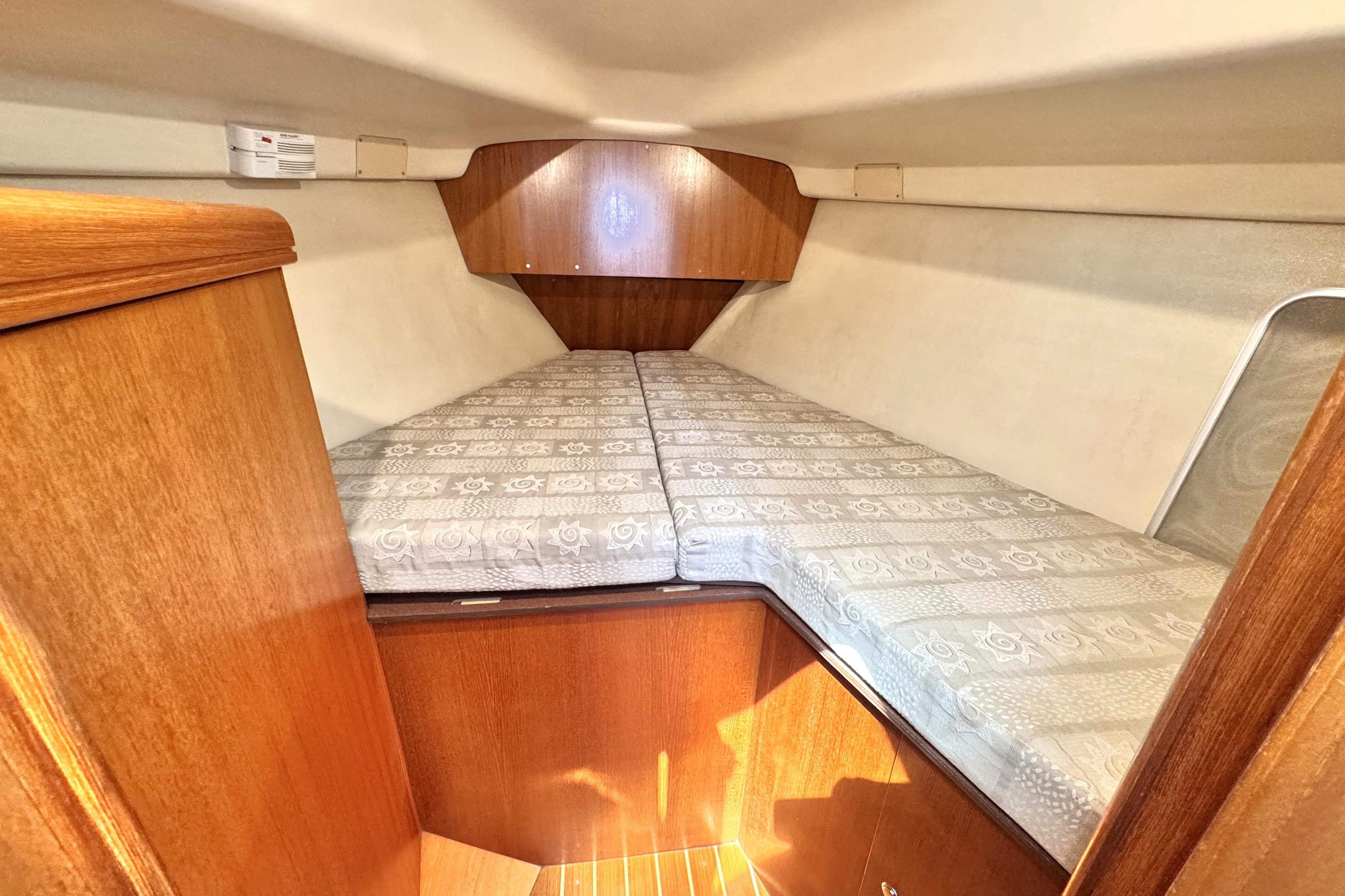 Cozy cabin interior of 2002 Hunter 326 sailboat with wooden finish and patterned cushions.