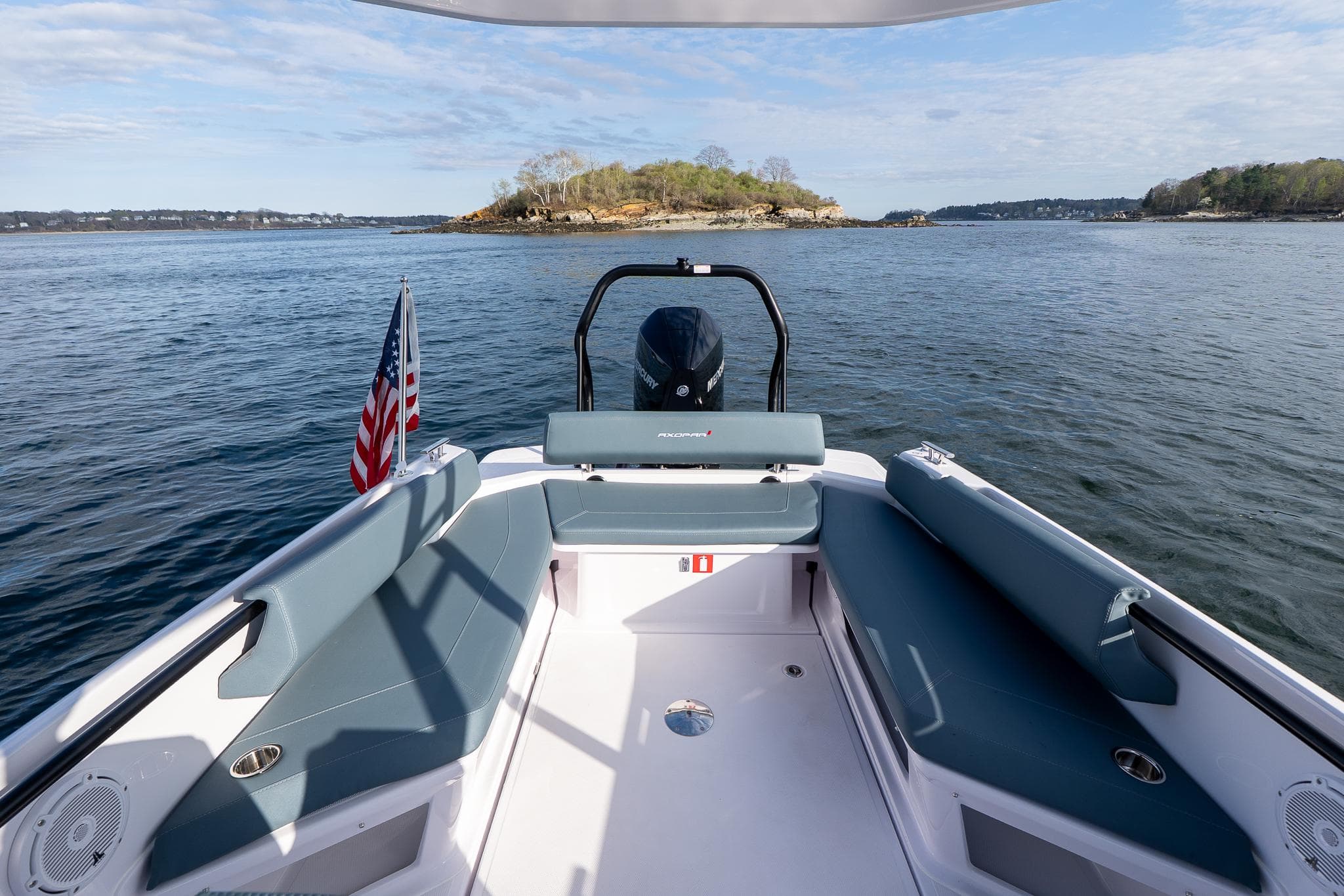 2025 Axopar Cross Top boat with seating, American flag, and scenic water view.