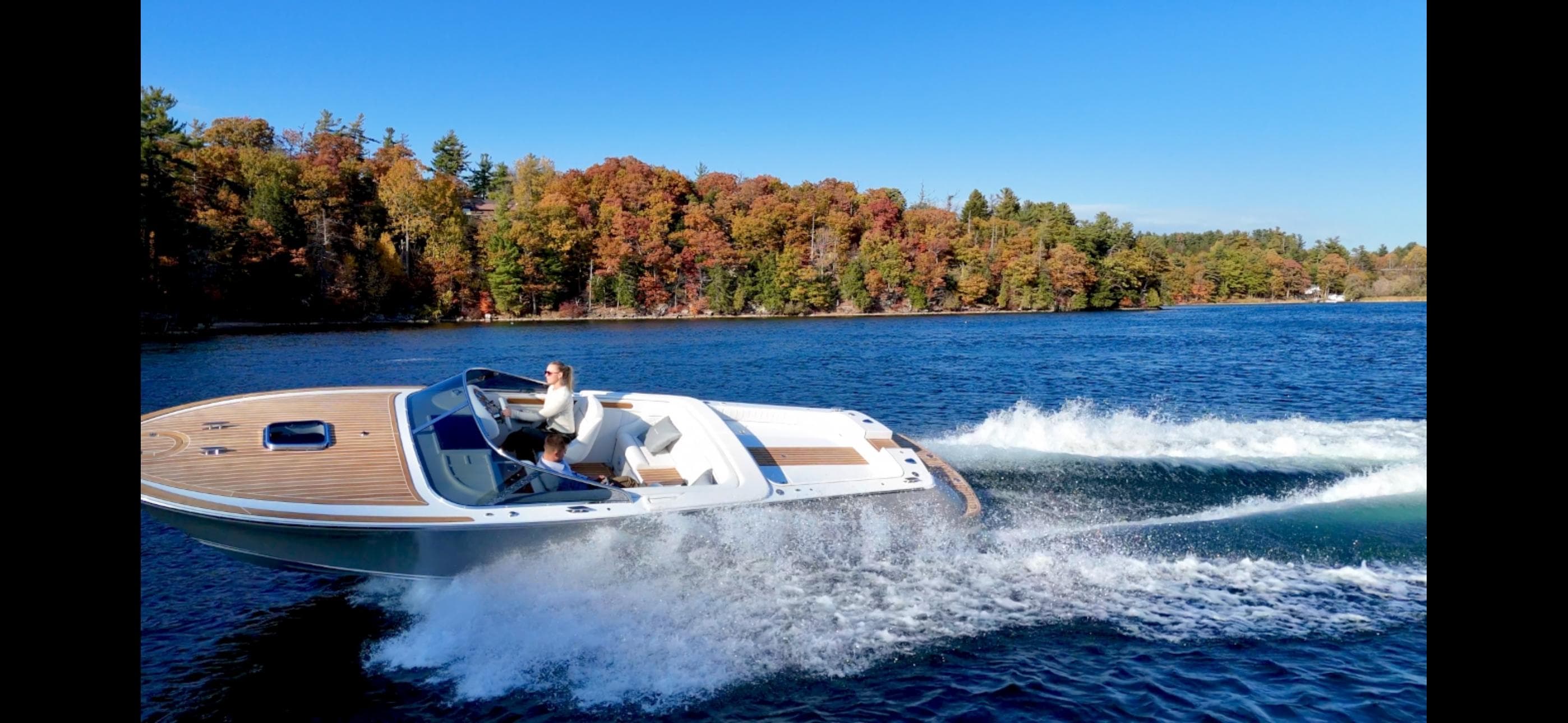 2024 Comitti Venezia V28 speedboat cruising on a lake with autumn foliage backdrop.