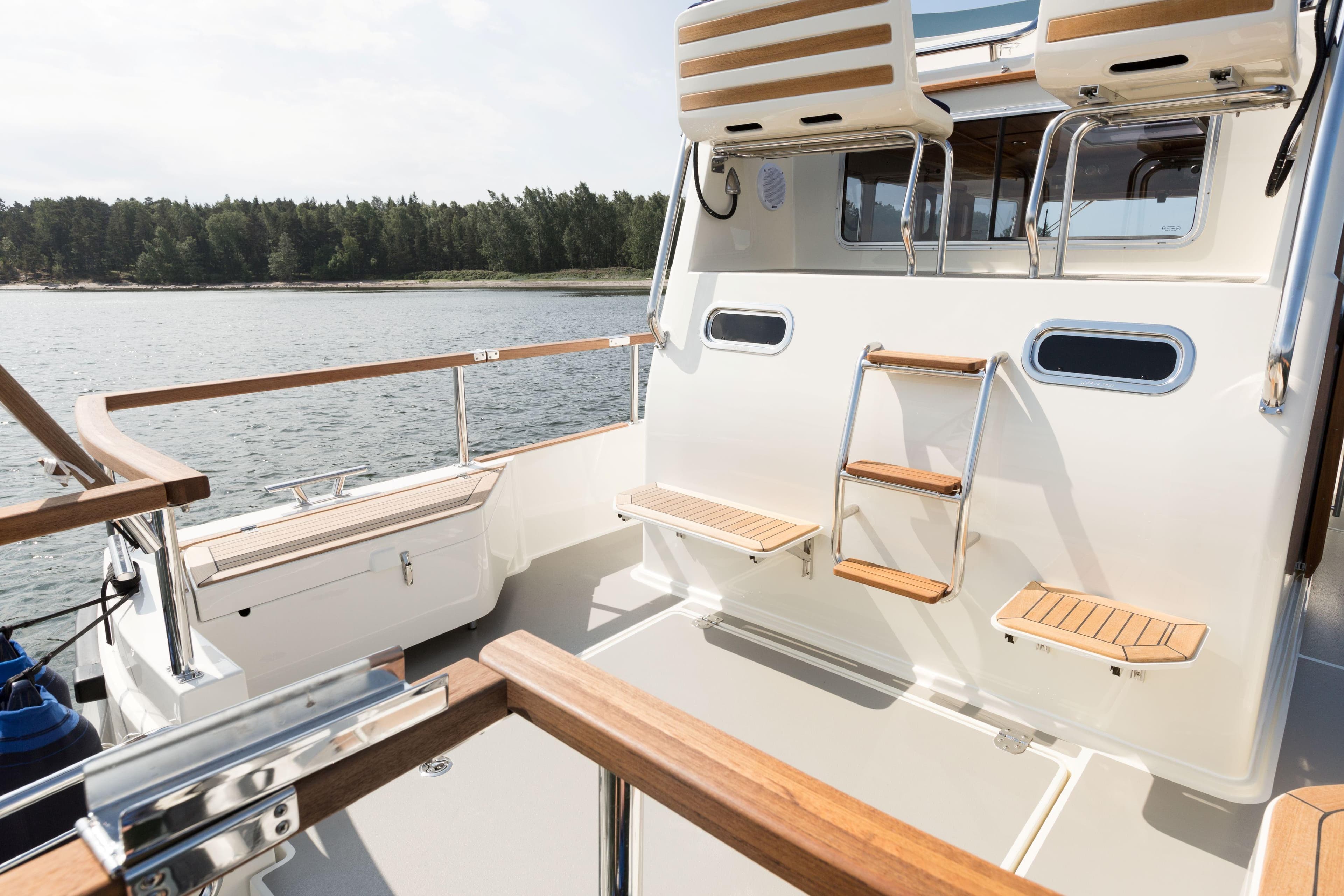 2026 Targa 27.2 boat deck with wooden accents and ladder, near scenic shoreline.