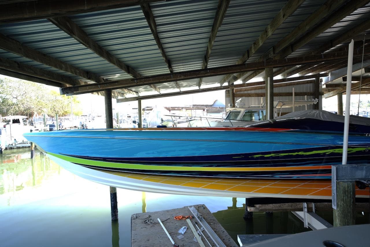 2008 Outerlimits 39 Quattro speedboat with vibrant stripes docked under a covered marina.