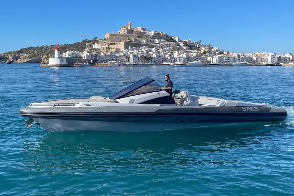 2008 SACS Strider boat cruising near a coastal city with a historic hilltop view.