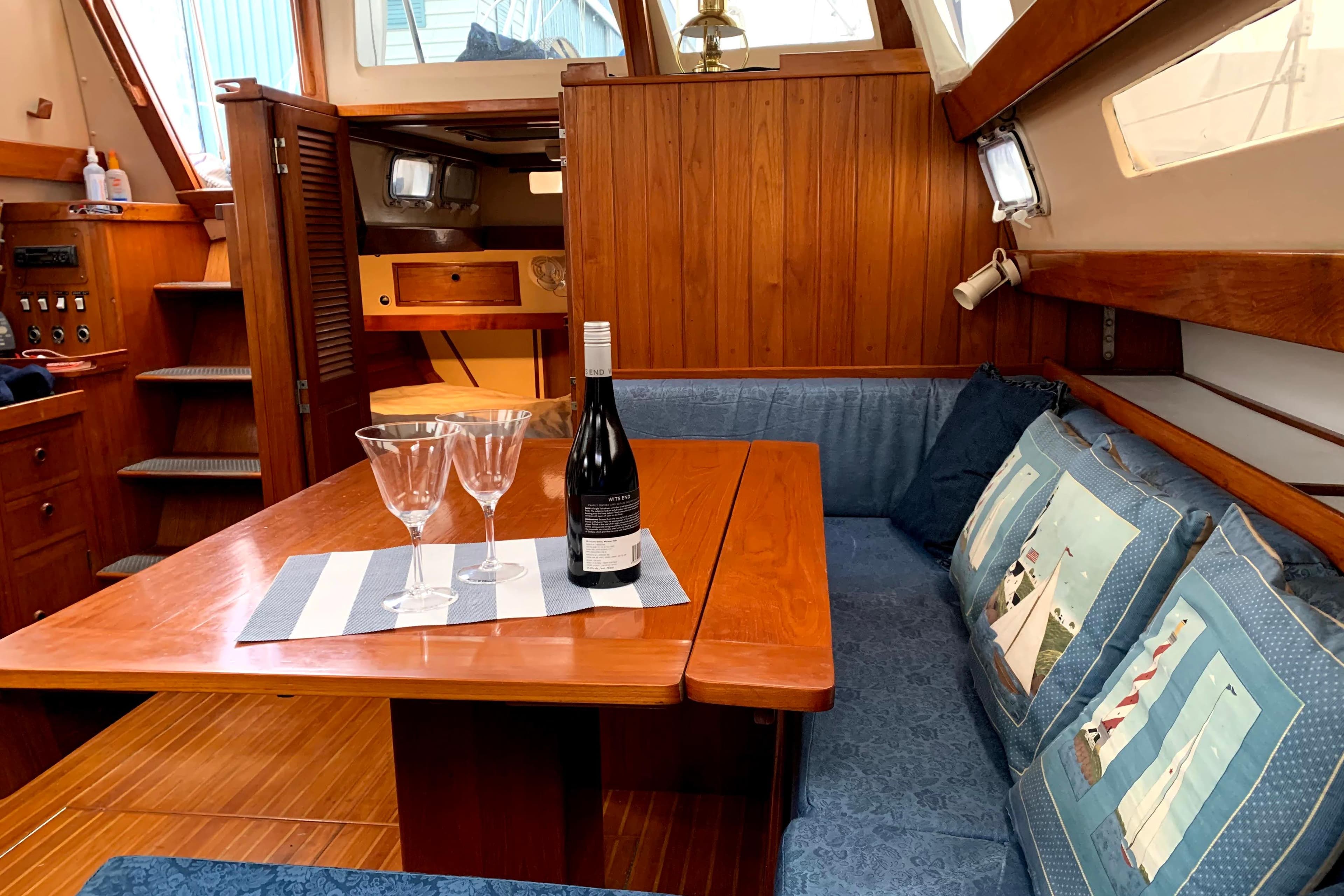 Interior of 1982 C&C Landfall 48 yacht with wooden table, wine, and nautical-themed cushions.