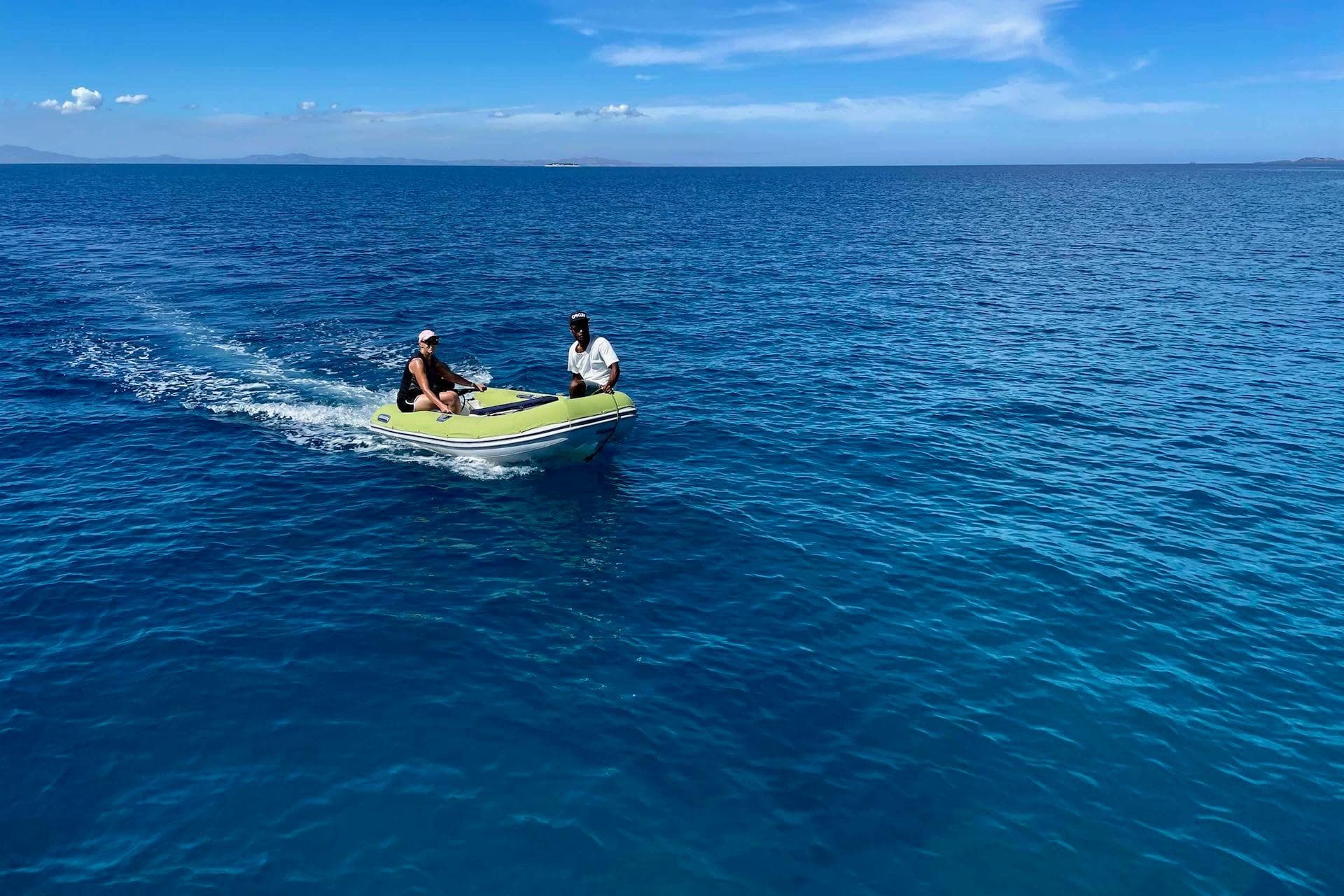 Two people on a small boat in clear blue ocean under a sunny sky.