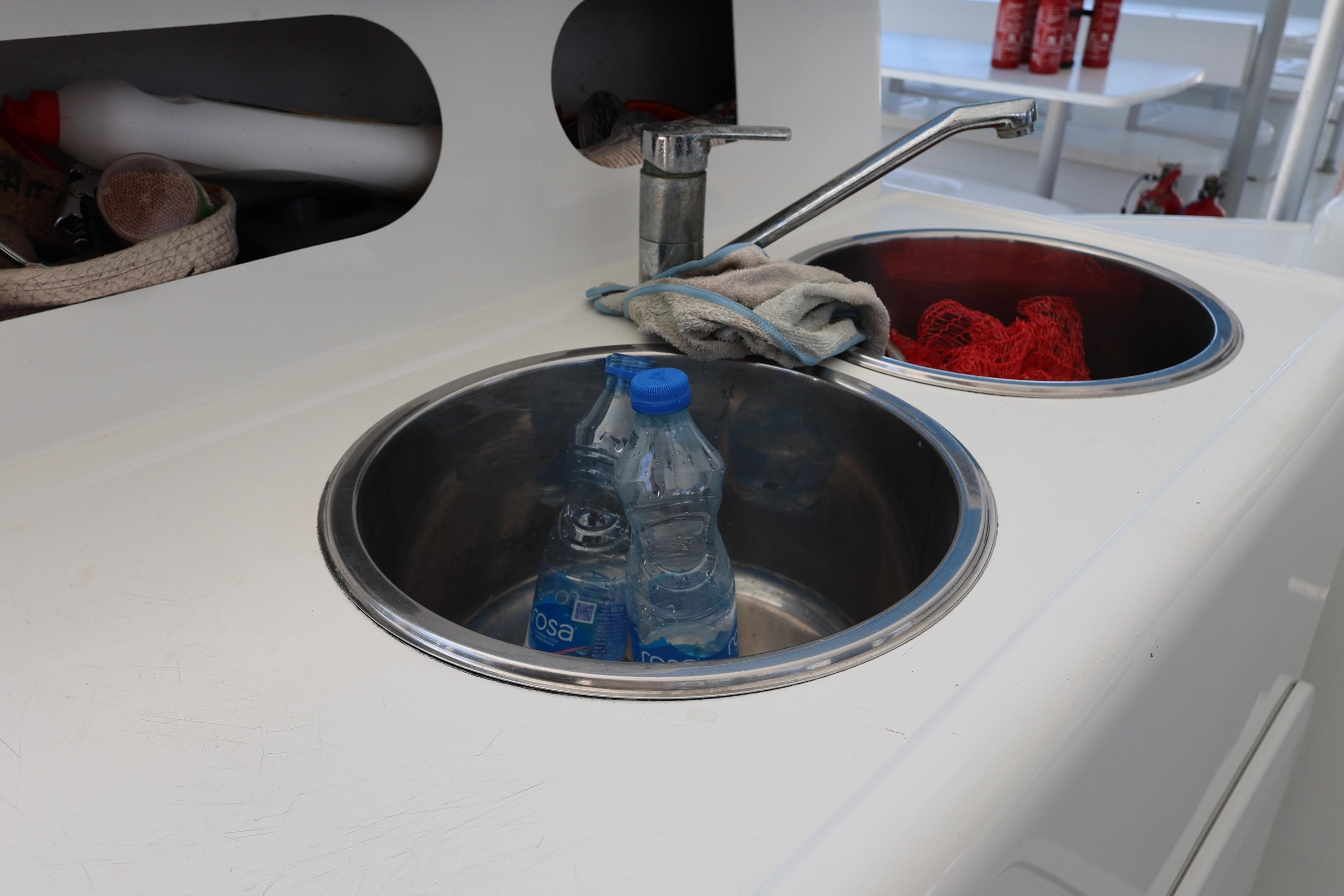 Sink area on 2015 Fountaine Pajot Taiti Day Charter 80 with water bottles and cleaning supplies.