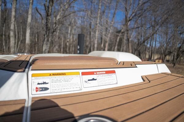 2017 Correct Craft Super Air Nautique GS boat deck with warning labels, surrounded by trees.