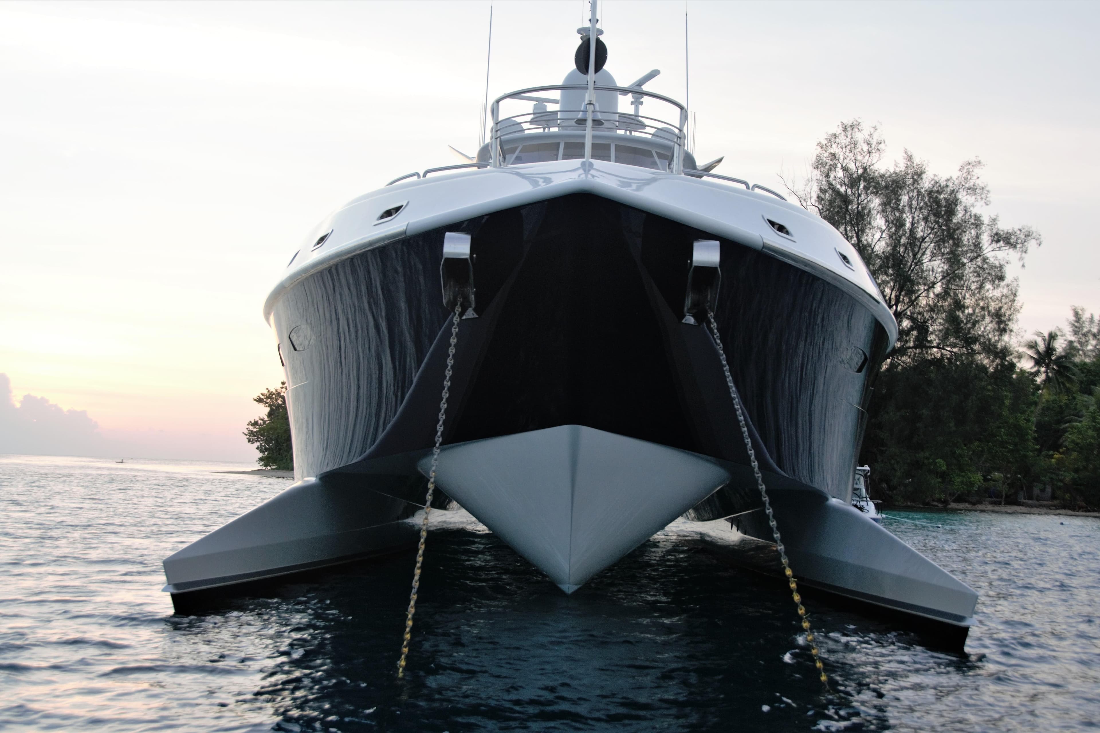 Luxury 2005 New Zealand Yachts 115 Wave Piercer at sunset, anchored near lush shoreline.