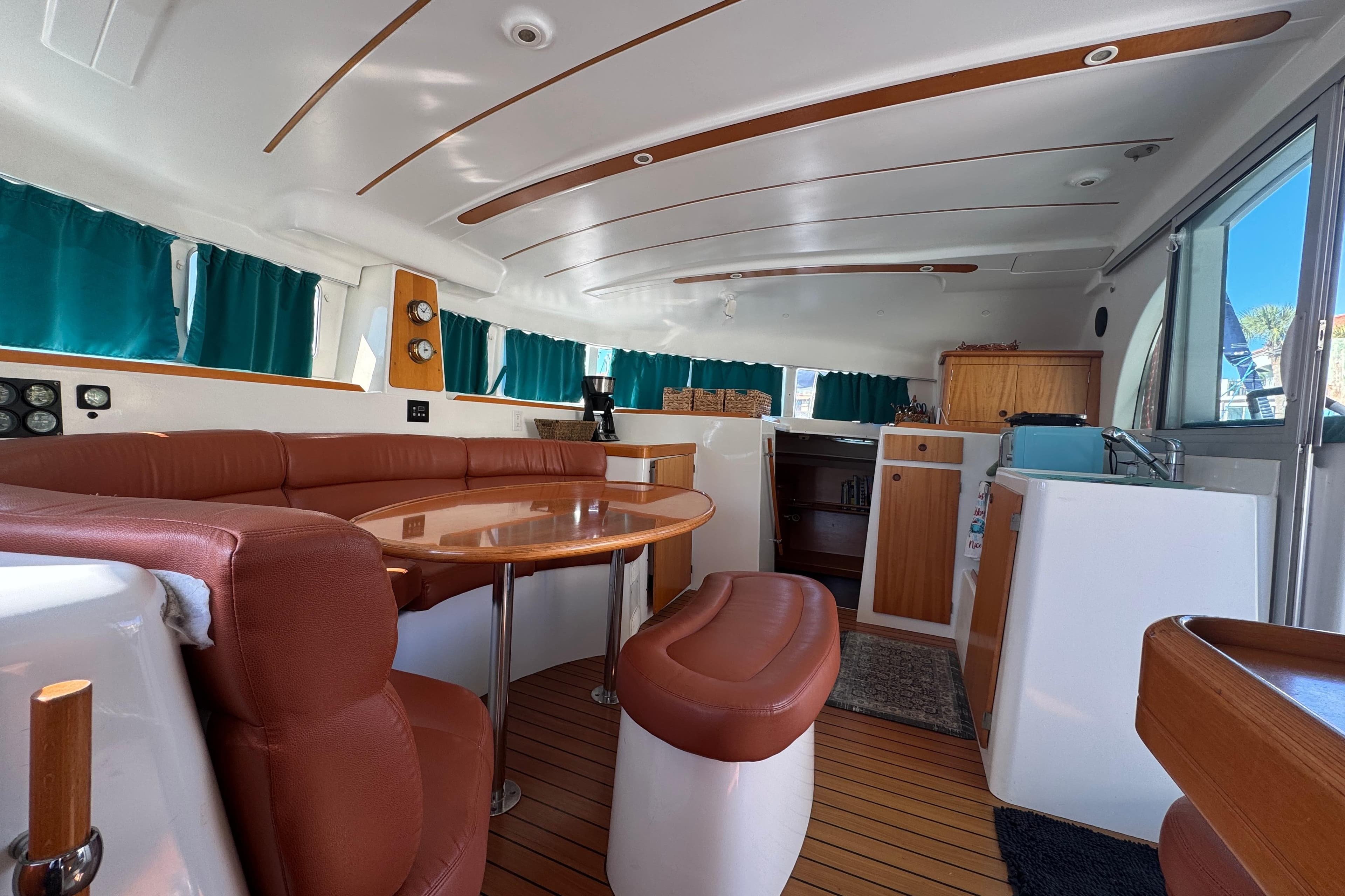 Interior of 2000 Lagoon 380 catamaran with brown seating, wooden table, and teal curtains.