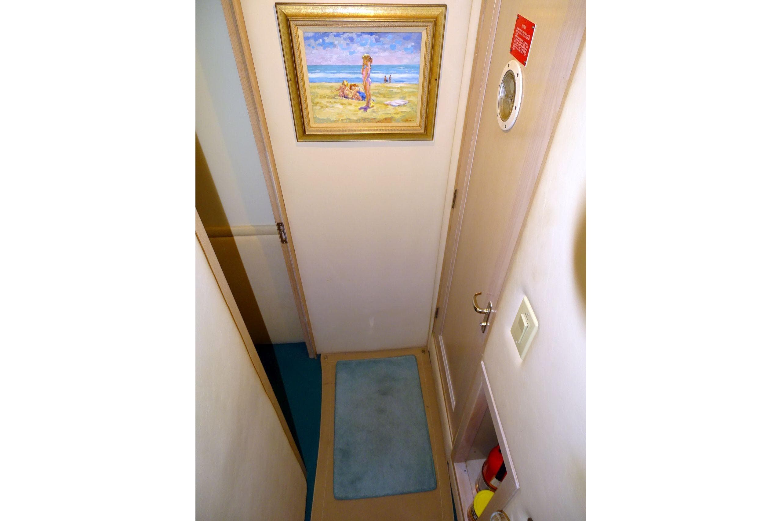 Narrow hallway in 1991 Hatteras 61 Motor Yacht with beach painting and blue rug.