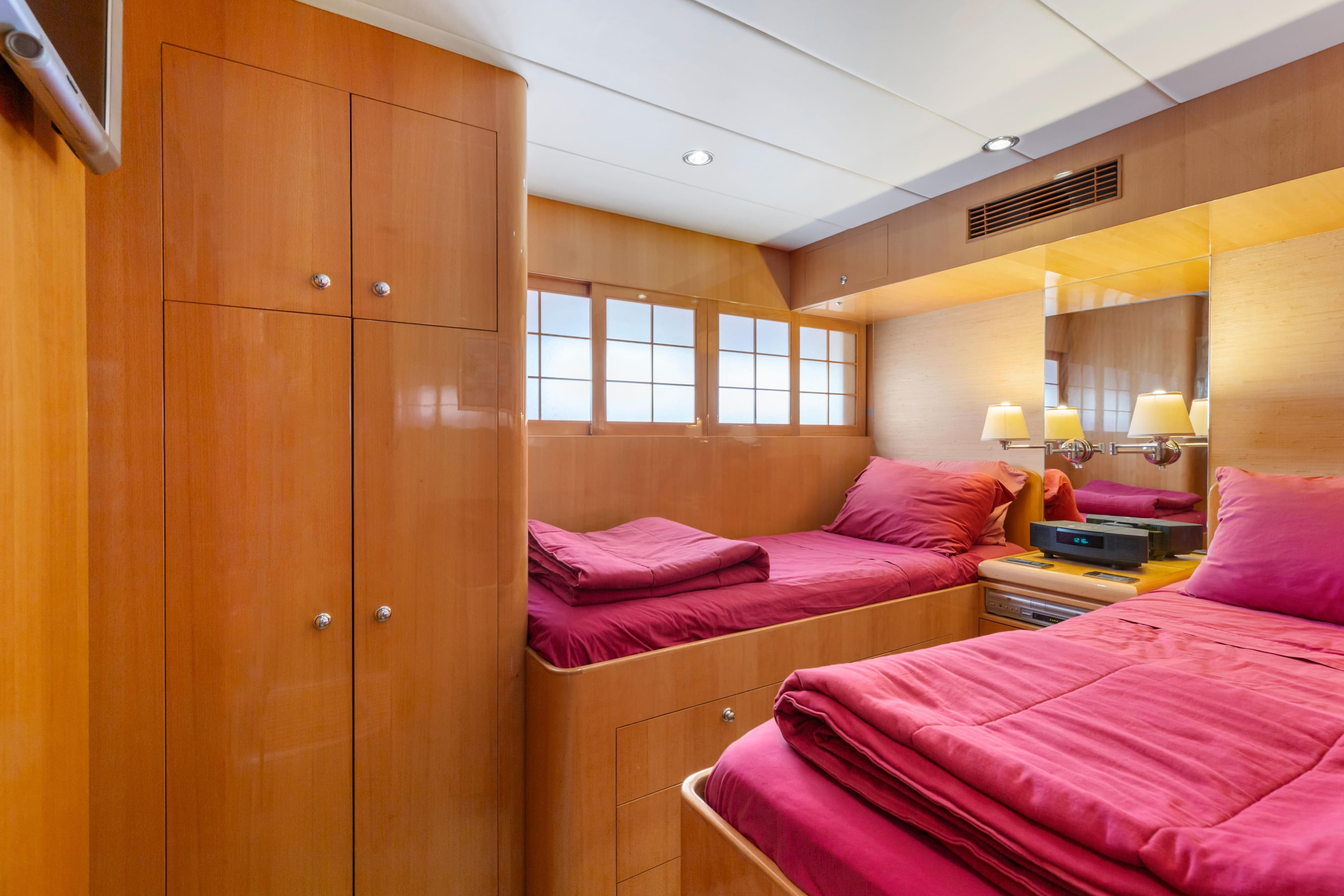 Luxurious 2005 C Custom yacht bedroom with twin beds, wooden cabinetry, and vibrant red bedding.