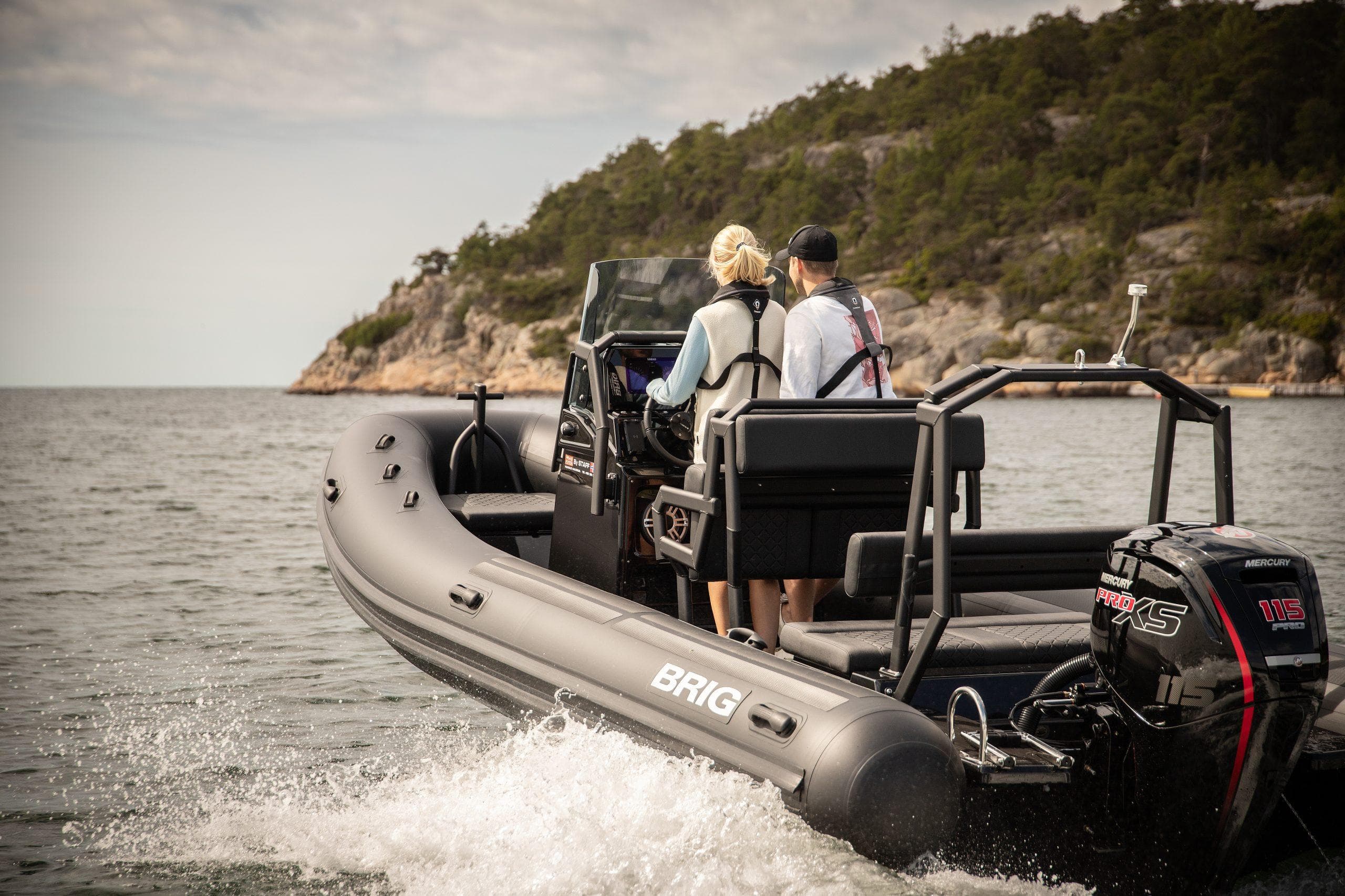 2026 Brig Navigator 20 boat cruising near rocky shoreline with two passengers.