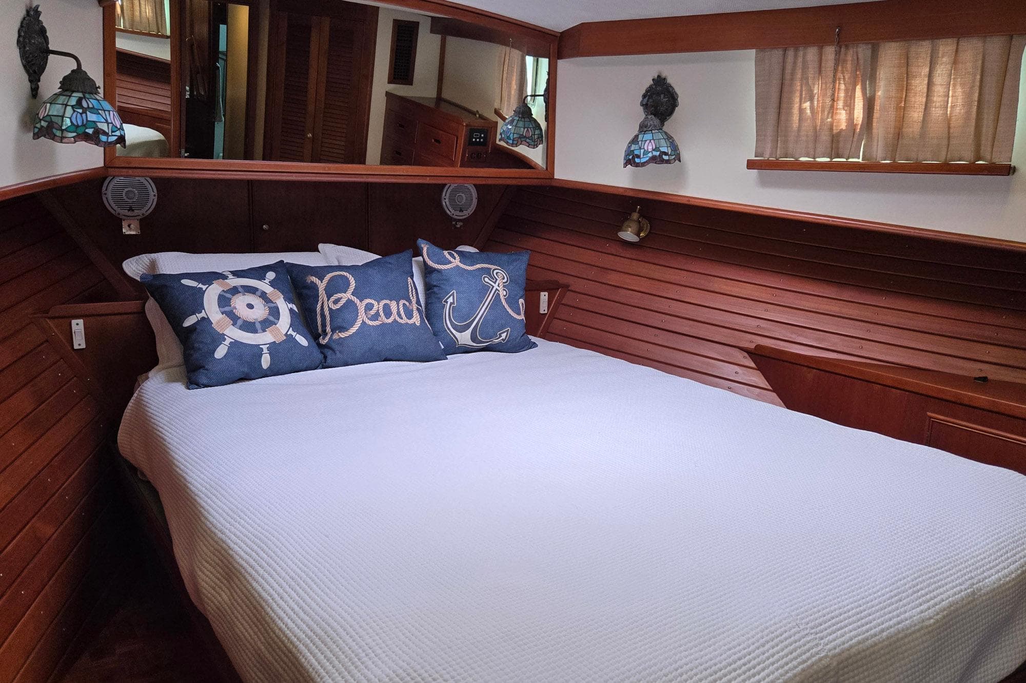 Cozy bedroom in 1997 Grand Banks 46 Europa yacht with nautical-themed pillows and wooden paneling.