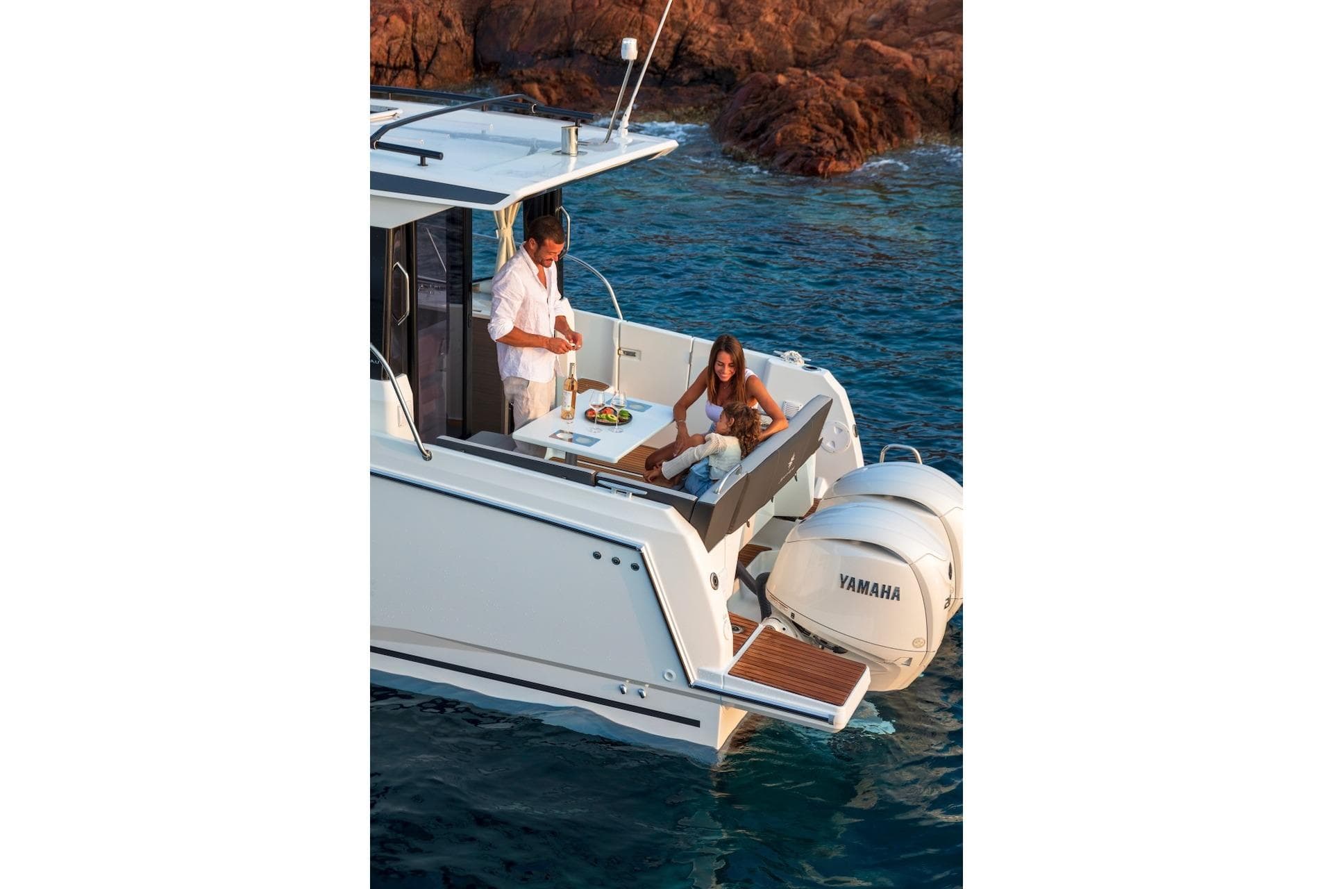 Couple enjoying leisure time on Jeanneau NC 895 Series 2 boat, 2025 model, near rocky shore.