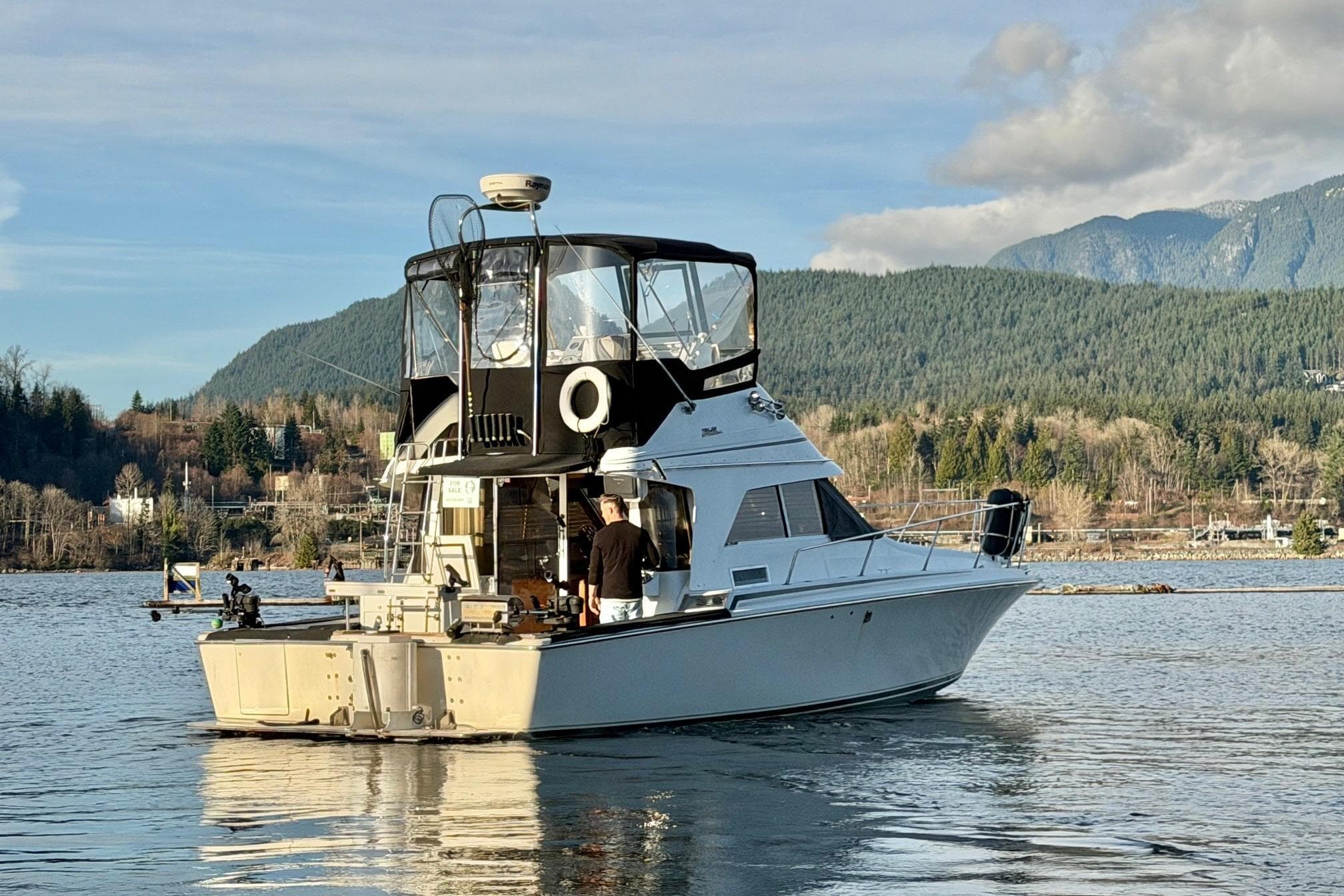 1990 Trojan 10.8 Meter Sedan boat on a scenic lake with mountains in the background.