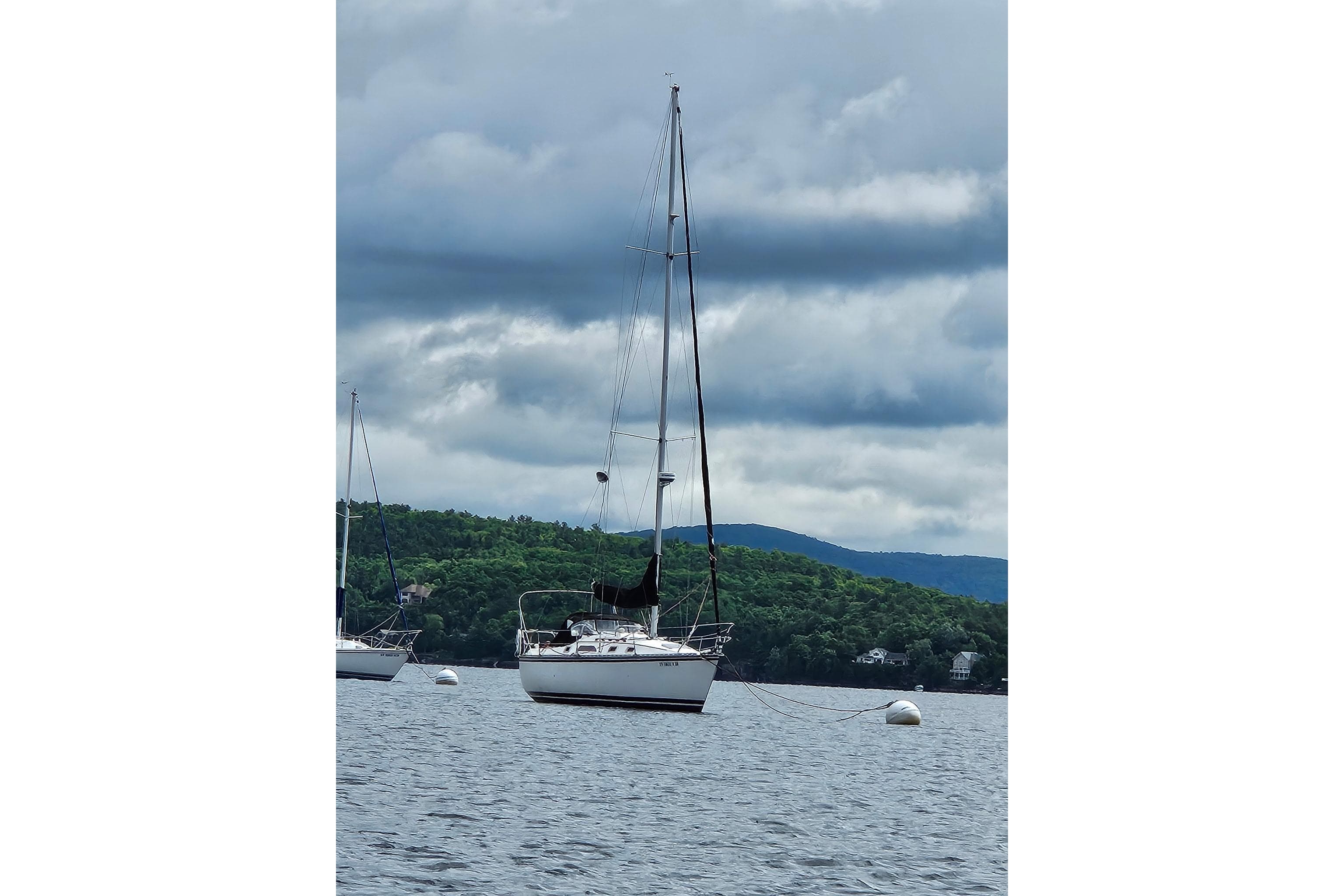 1985 Hunter 31 sailboat anchored on a lake with cloudy skies and lush green hills.