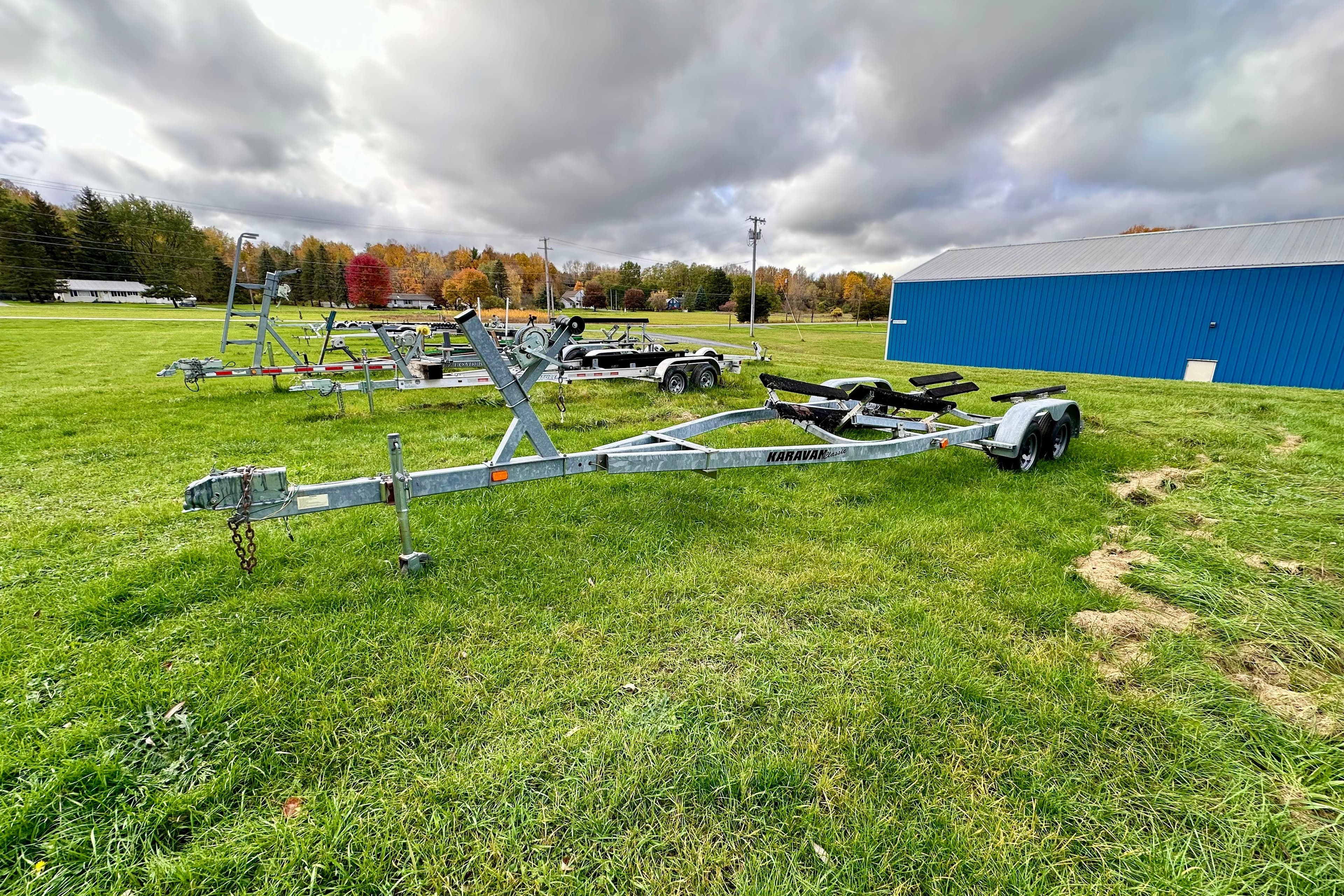 Boat trailers on grassy field near blue building, overcast sky. Chris-Craft Corsair 25, 2003.