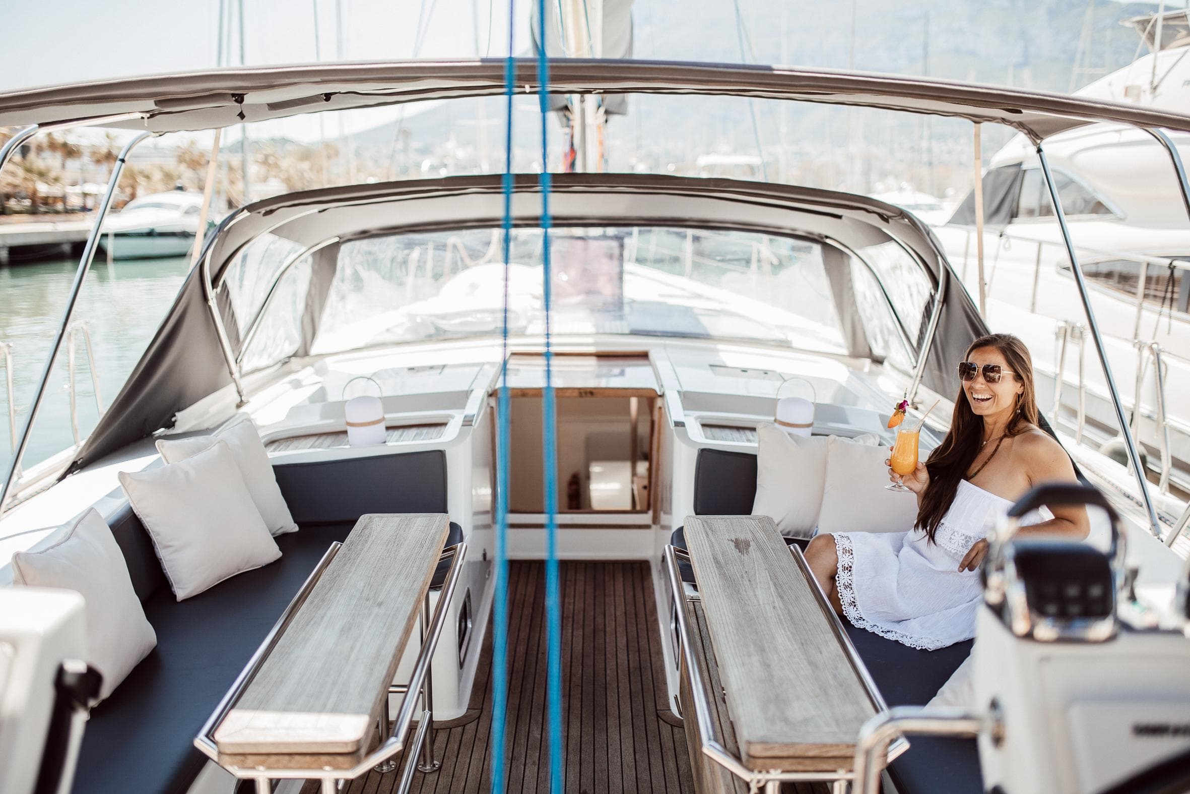 Woman relaxing on 2008 Hanse 630e yacht, enjoying a drink in the sunlit cockpit.