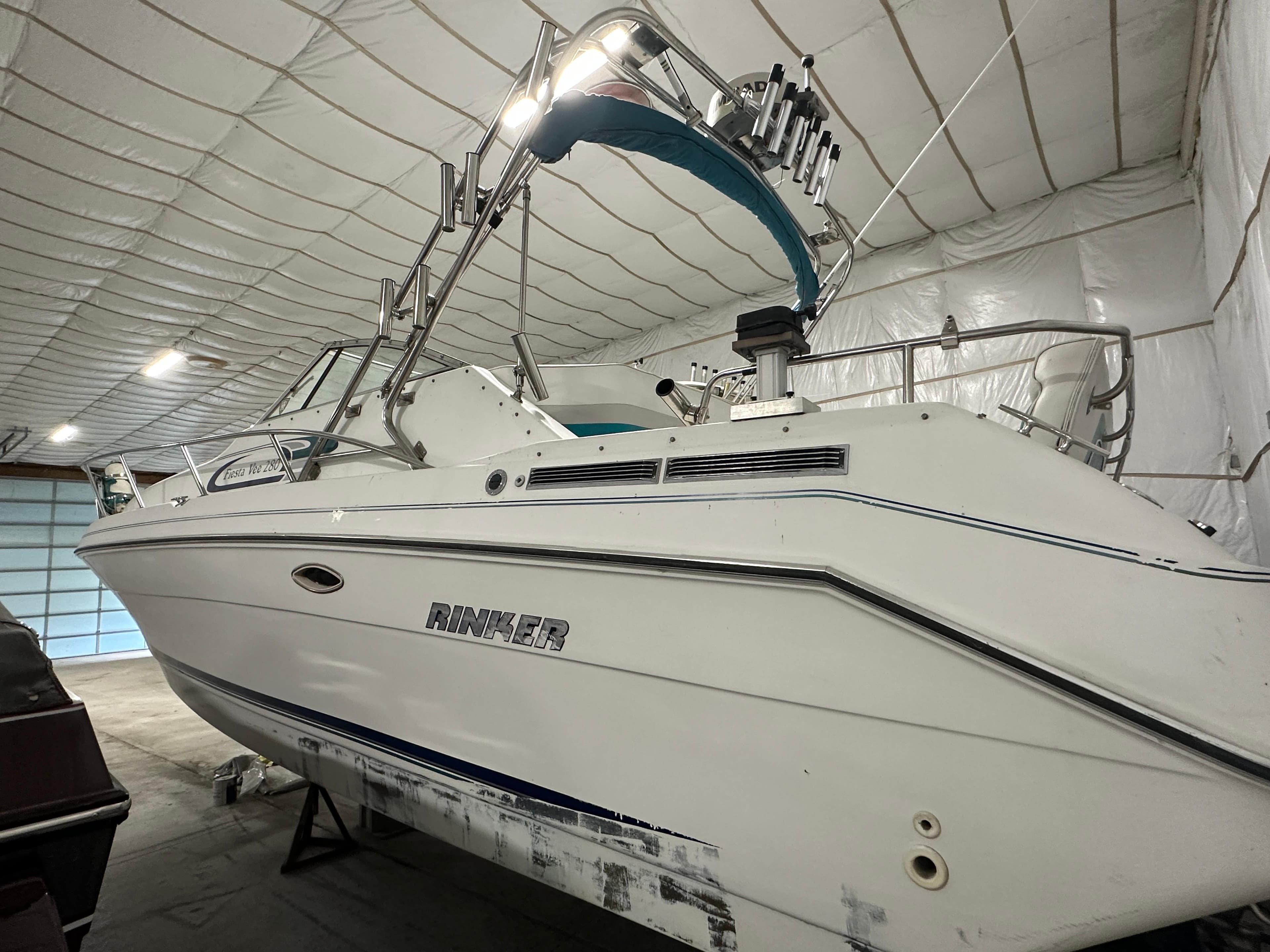 1993 Rinker 280 Fiesta Vee boat in indoor storage, white hull, blue accents.