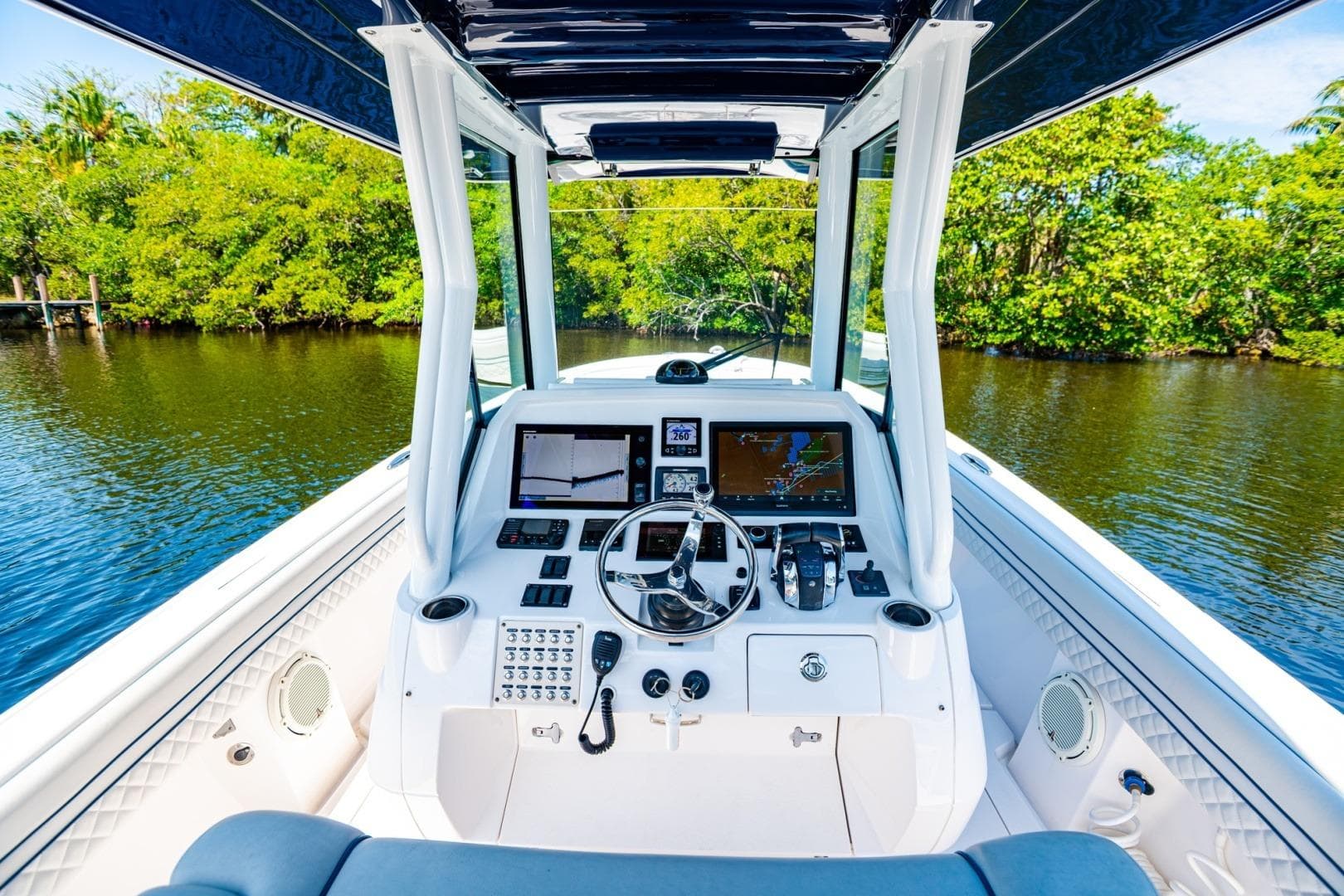 2018 Intrepid 327 Center Console boat cockpit with navigation screens, steering wheel, and lush waterway view.