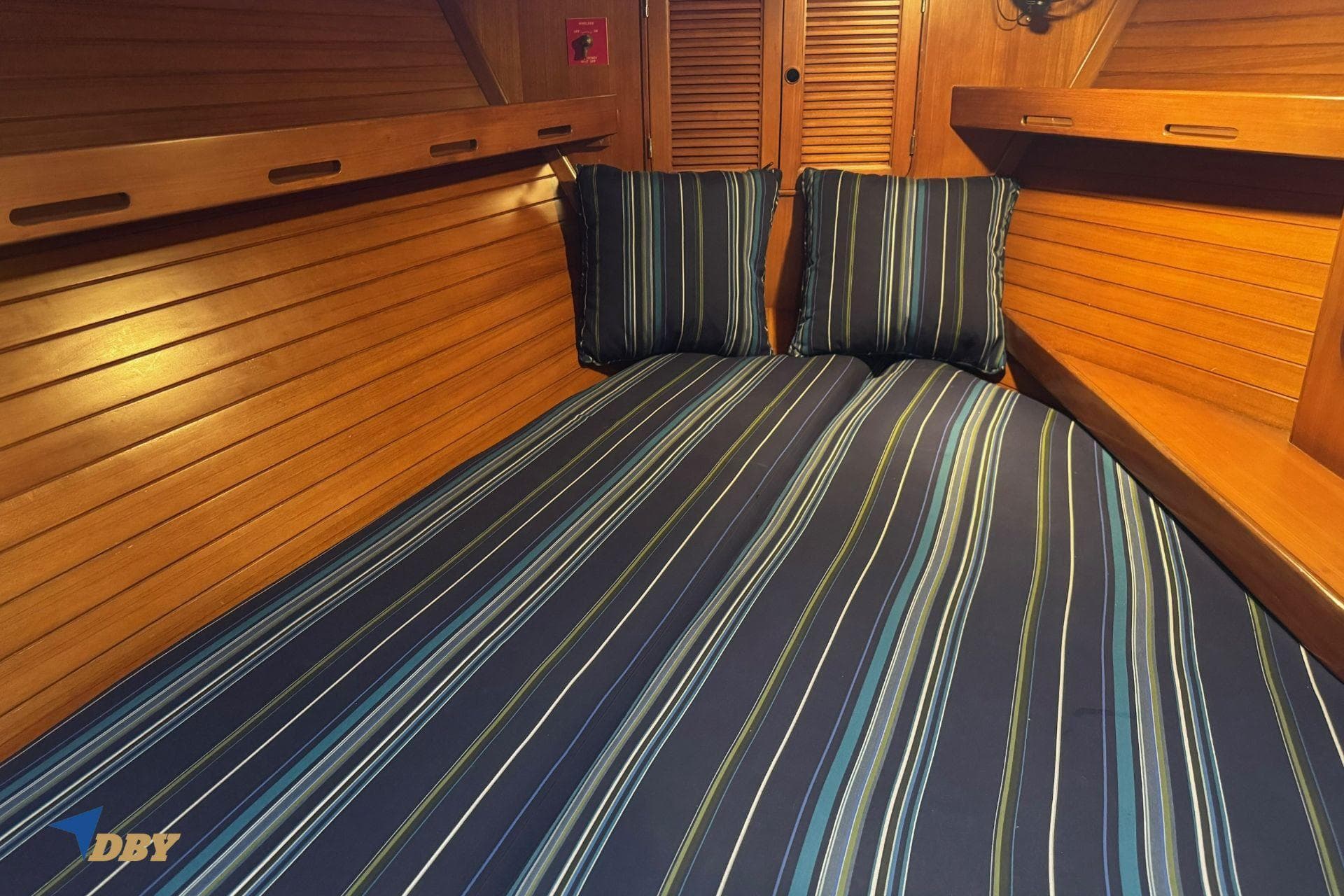 Cozy cabin interior of 1983 Mason 53 yacht with striped bedding and wooden paneling.