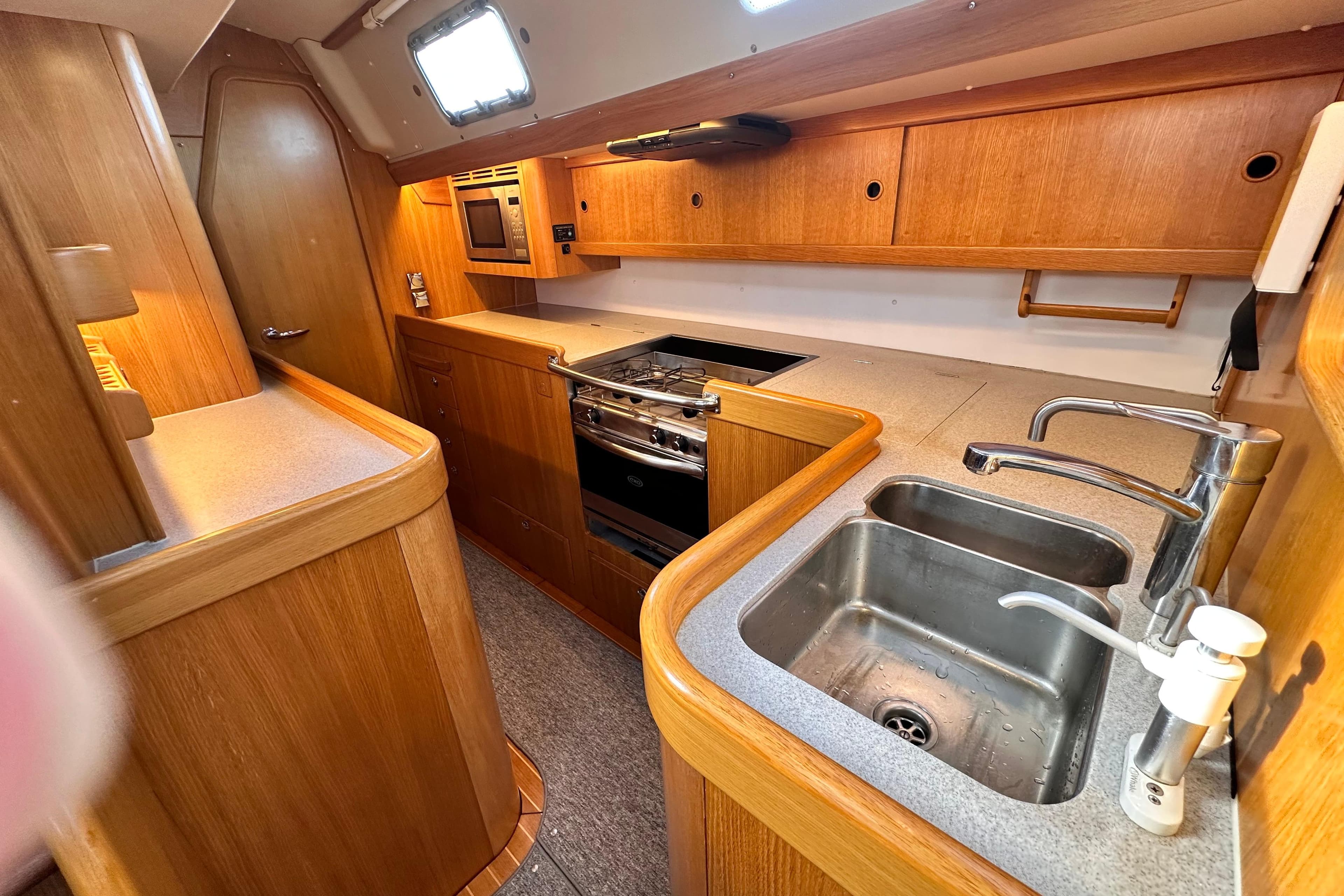 2019 Hallberg-Rassy 44 yacht kitchen with wooden cabinetry, dual sinks, and modern appliances.