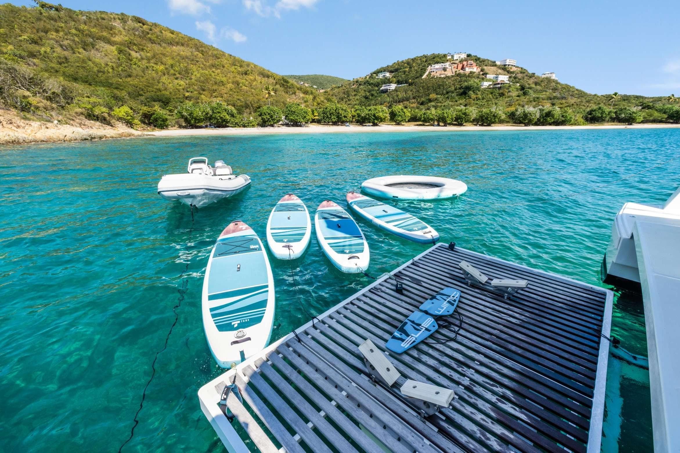 2023 Bali 5.4 Catamaran with paddleboards and inflatable in turquoise waters near lush island.