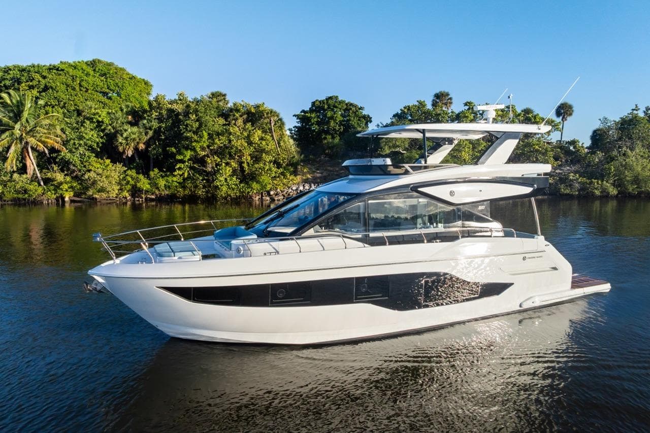 2026 Cruisers Yachts 50 Fly luxury yacht cruising on a serene river.