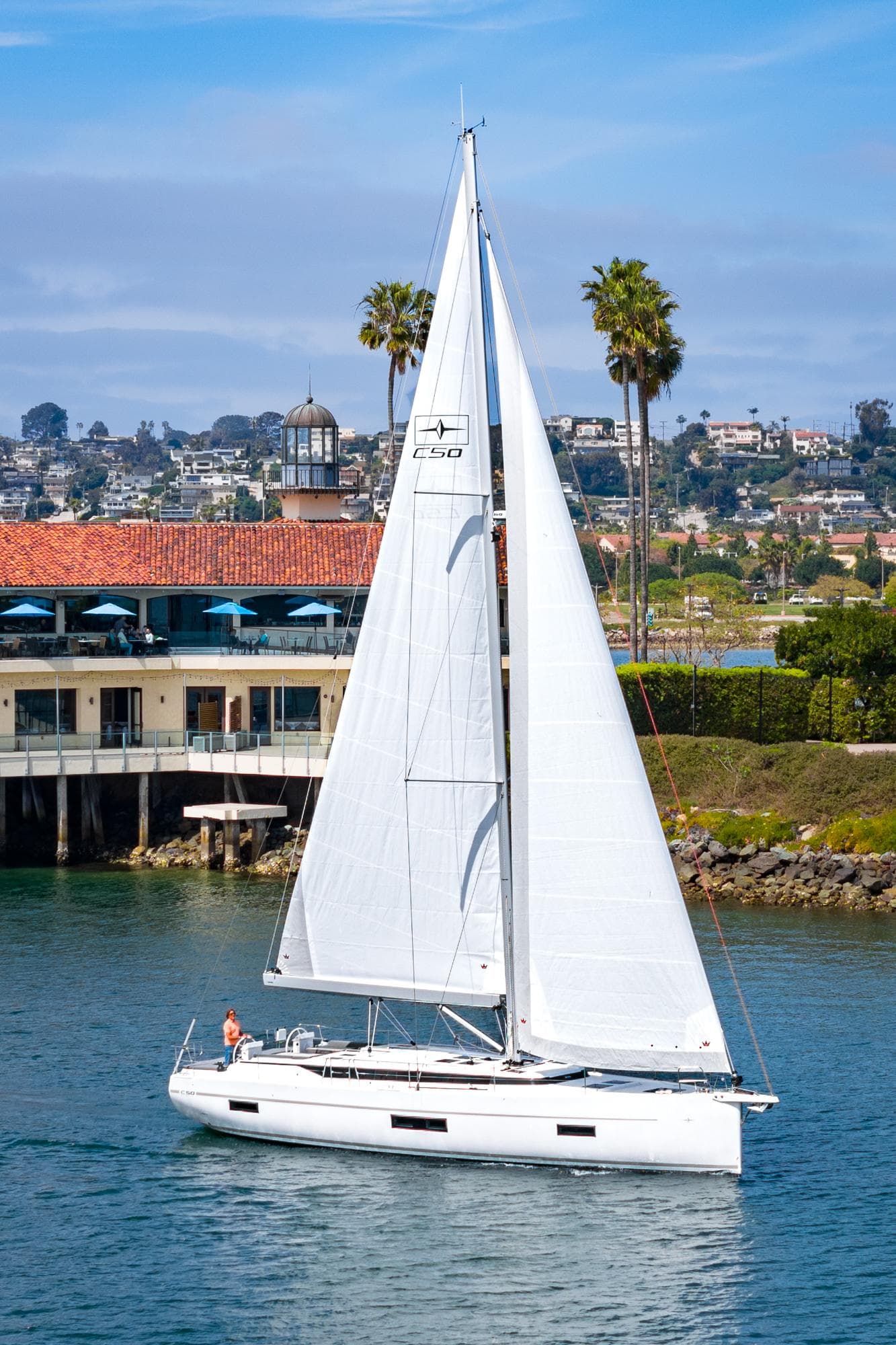 2024 Bavaria C50 sailboat cruising near coastal buildings and palm trees.