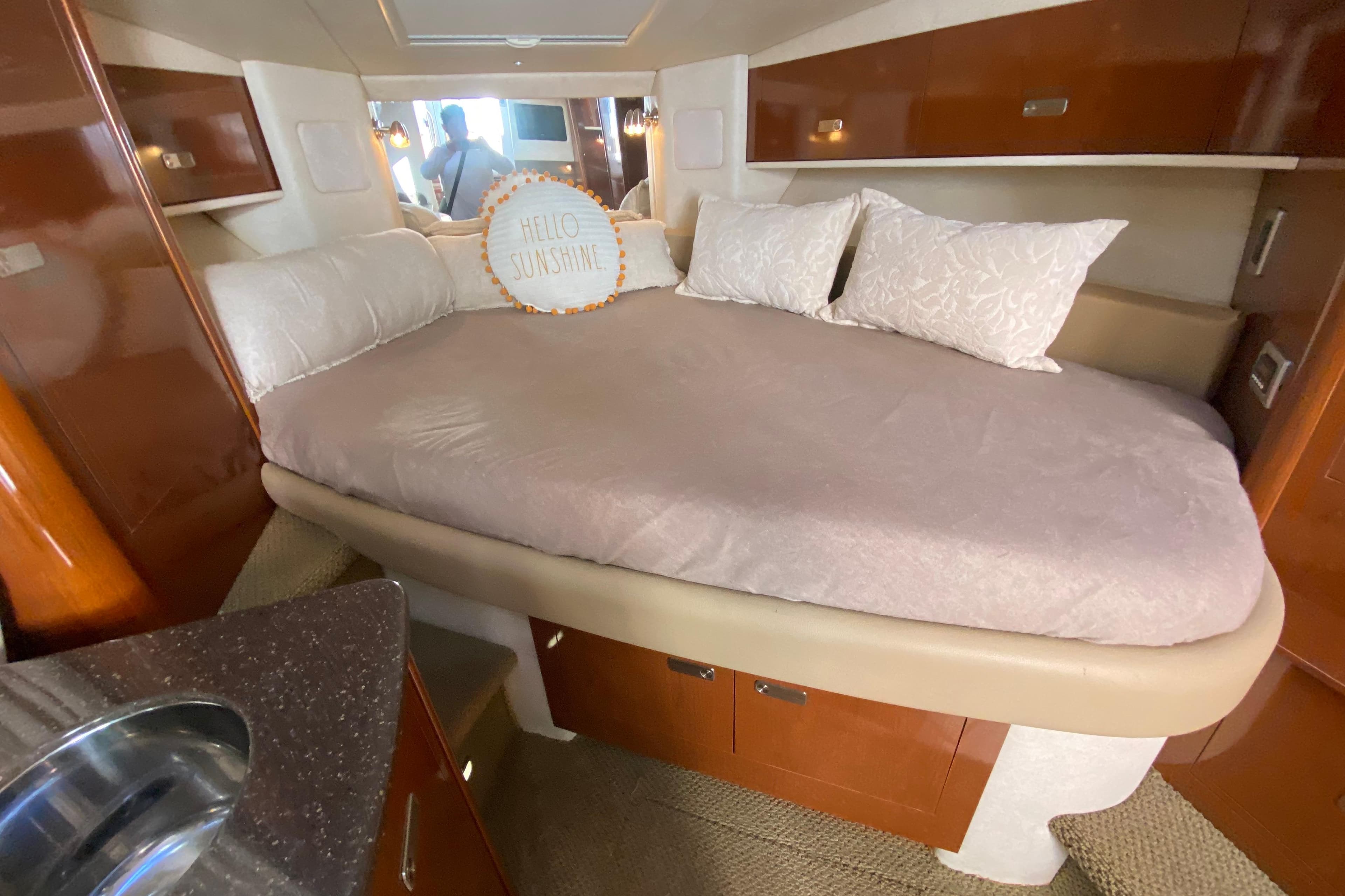 Cozy cabin interior of 2012 Sea Ray 330 Sundancer with plush bedding and "Hello Sunshine" pillow.