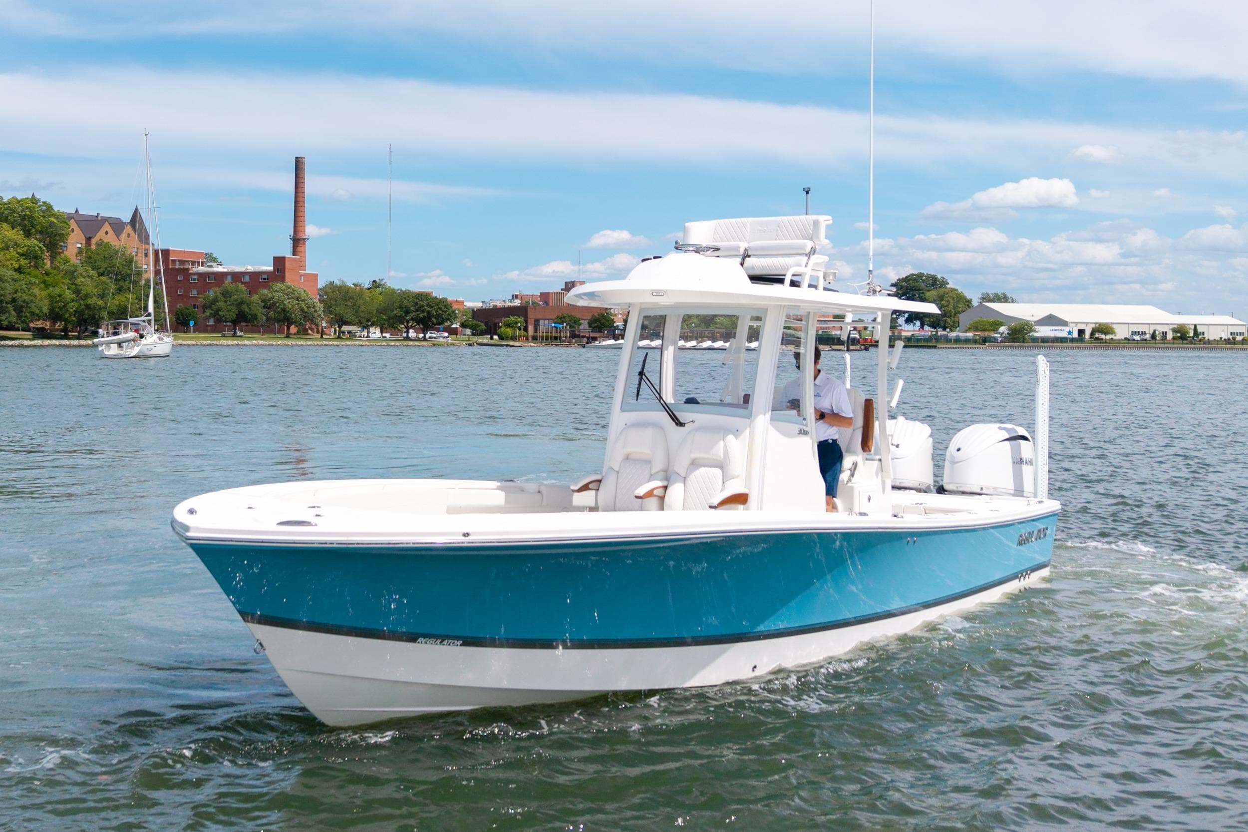 2023 Regulator 30XO boat cruising on a scenic waterway with buildings in the background.