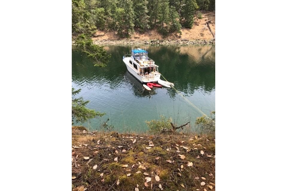 1983 Canoe Cove Sedan Bridge anchored in a serene forested lake setting.
