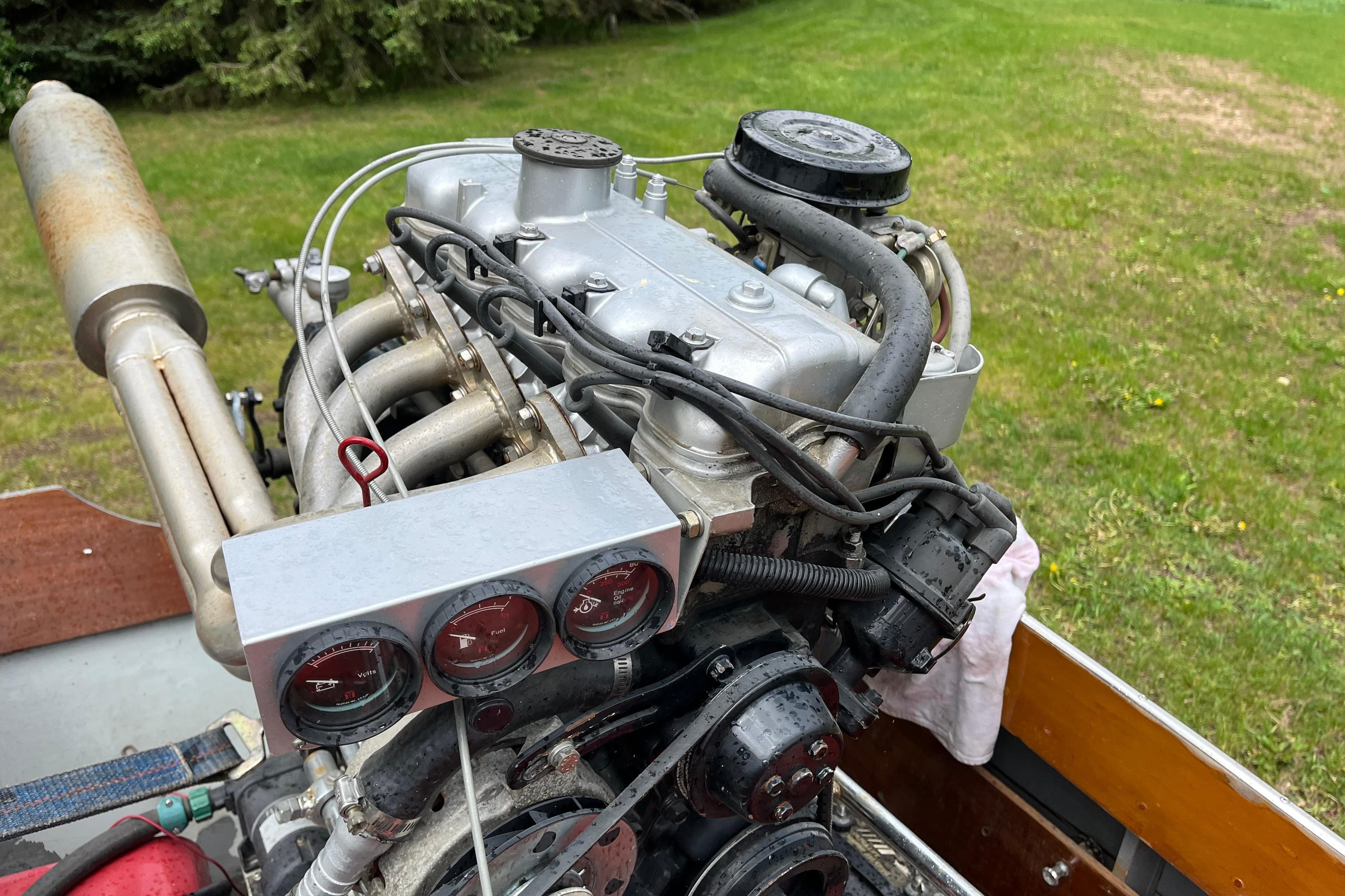 Close-up of a 1990 Thai Longboat utility engine with gauges, set against a grassy background.