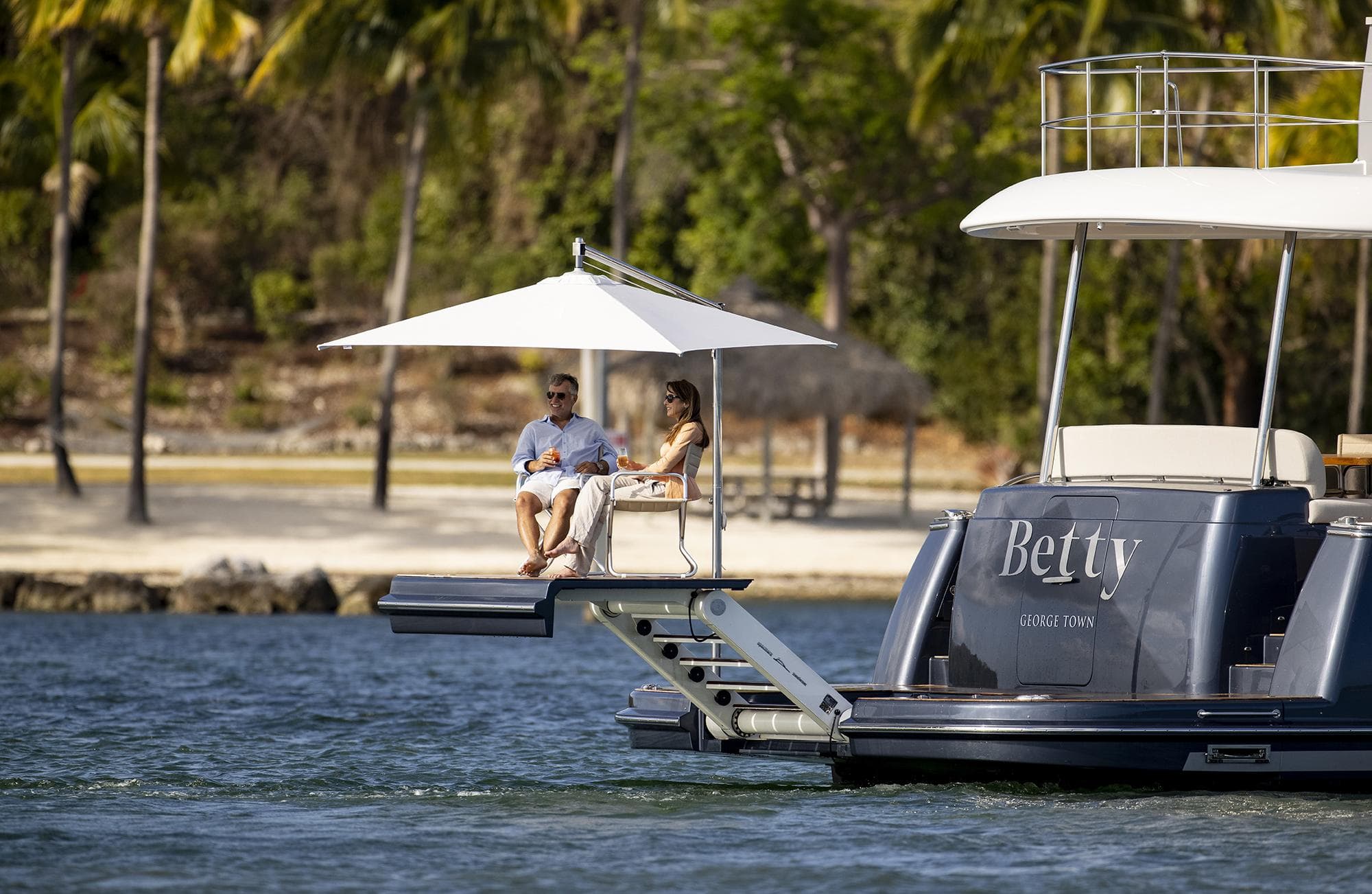 Couple relaxing on 2026 Grand Banks GB 85 yacht, enjoying waterfront view.