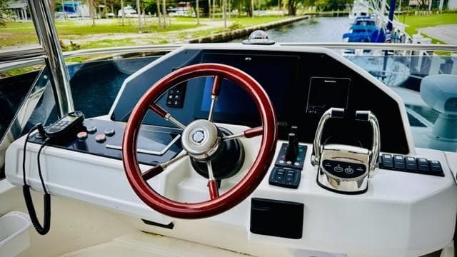 Helm of 2022 Greenline 48 Flybridge with Hardtop, featuring modern controls and red steering wheel.