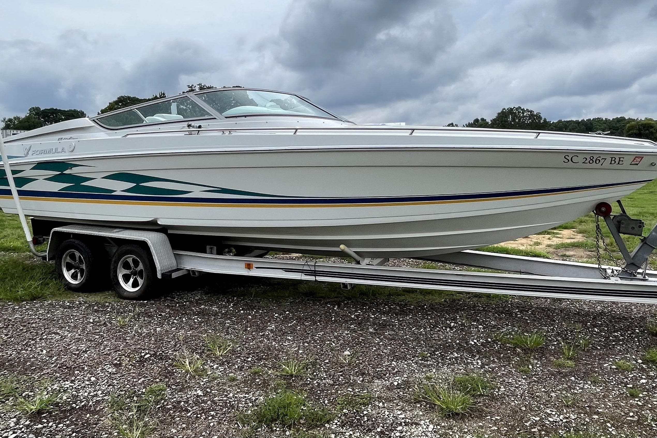1999 Formula 271 FASTech boat on trailer, parked outdoors under cloudy sky.
