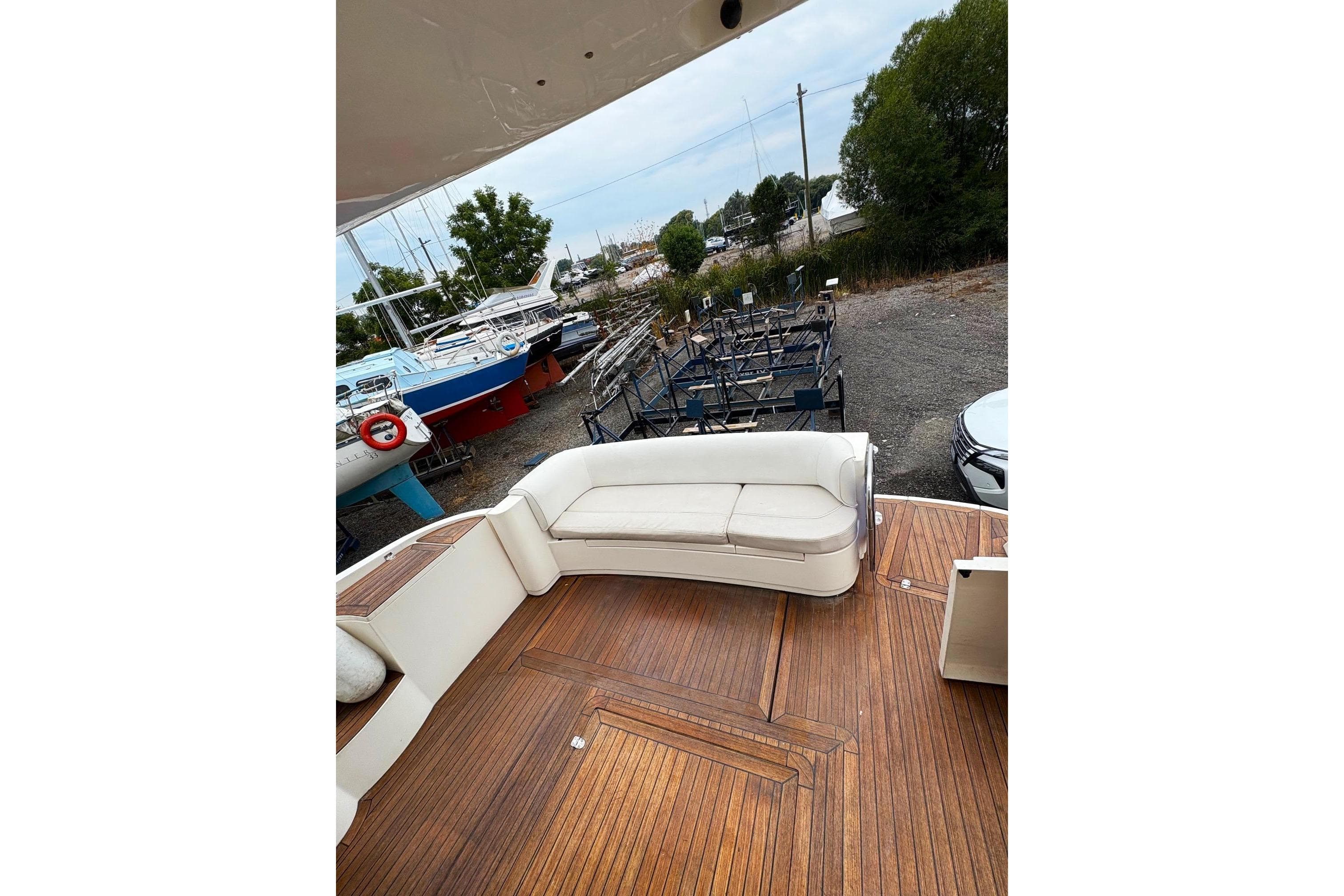 2003 Sealine F42/5 yacht with wooden deck and white seating, docked near other boats.