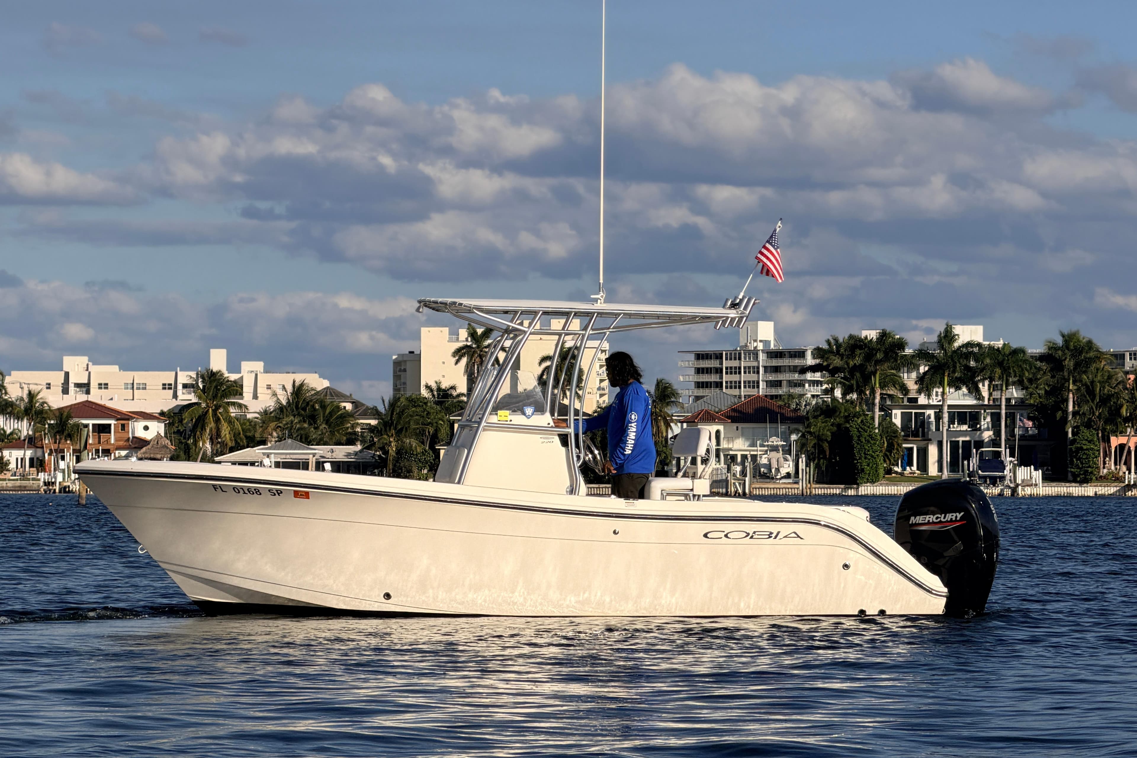 2020 Cobia 220 Center Console boat on water, cityscape background, American flag flying.