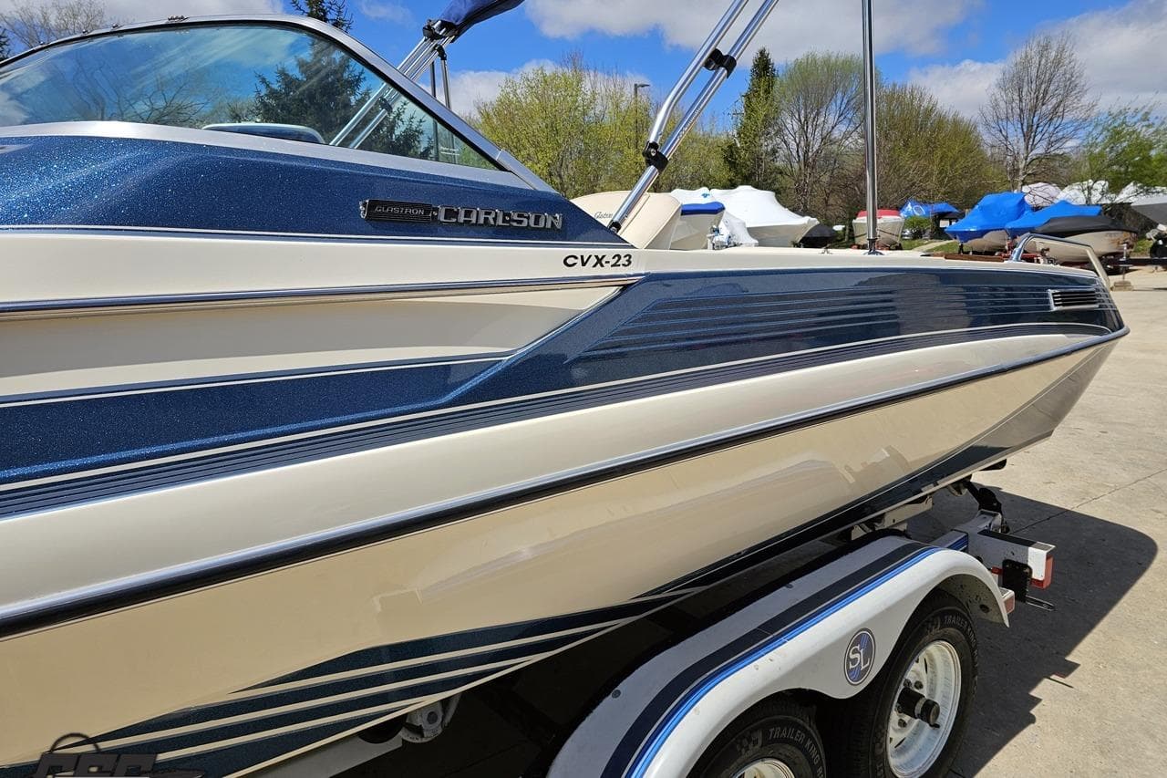 1988 Glastron/Carlson CVX-23 boat on trailer, blue and white design, parked outdoors.