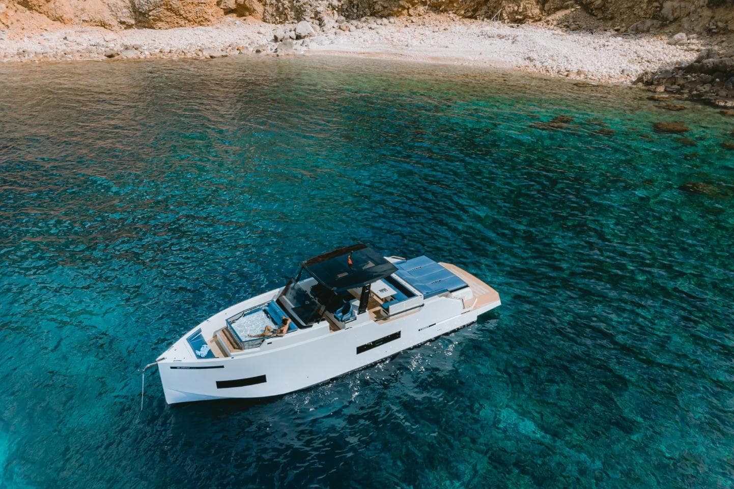```markdown
Luxurious 2026 De Antonio Yachts 50 Open cruising in clear turquoise waters near a rocky shoreline.
```