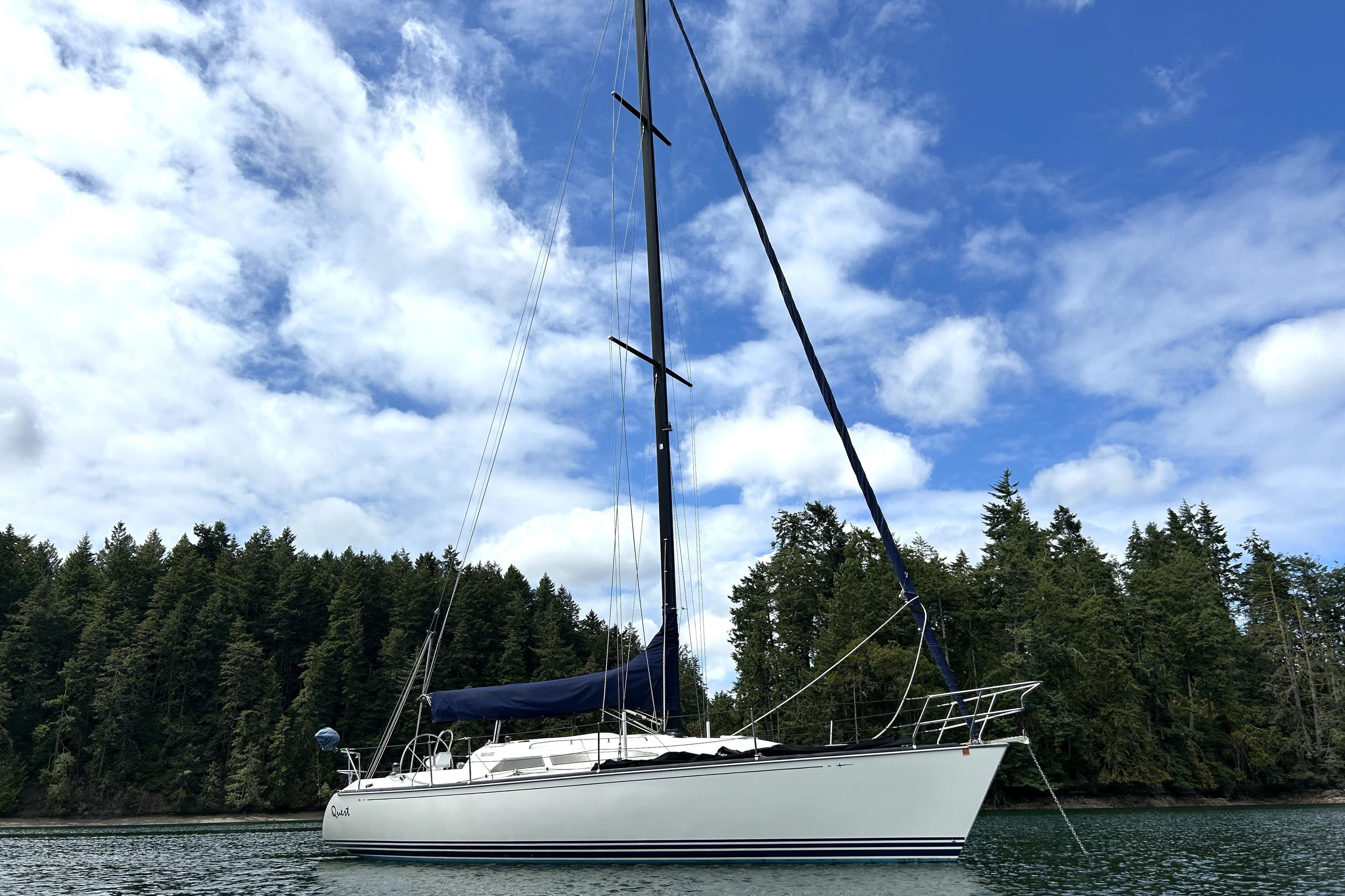 Sailboat C&C 110 (2004) on calm water with forested shoreline and cloudy sky.