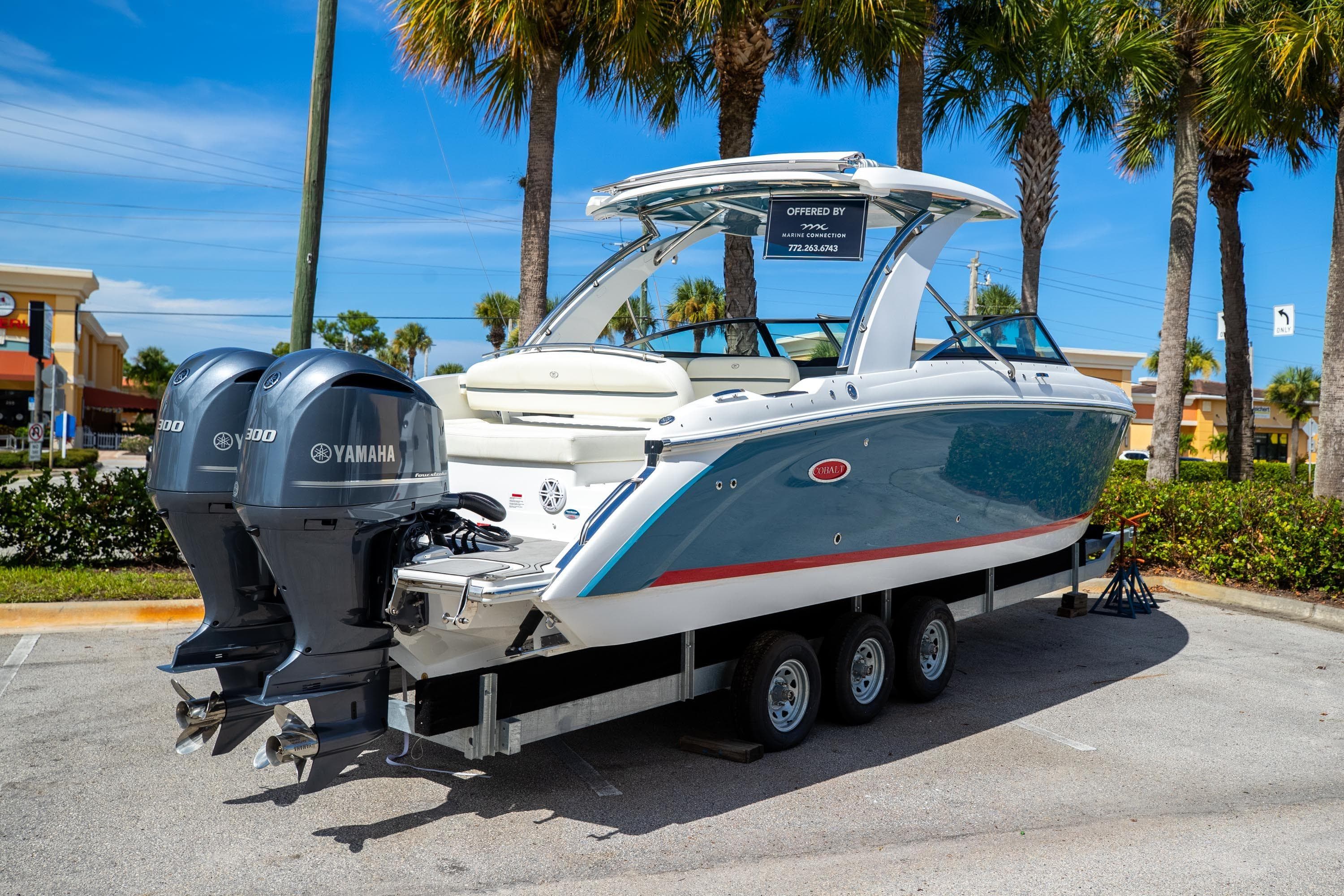 2022 Cobalt 30SC boat with Yamaha engines on a trailer, parked under palm trees.