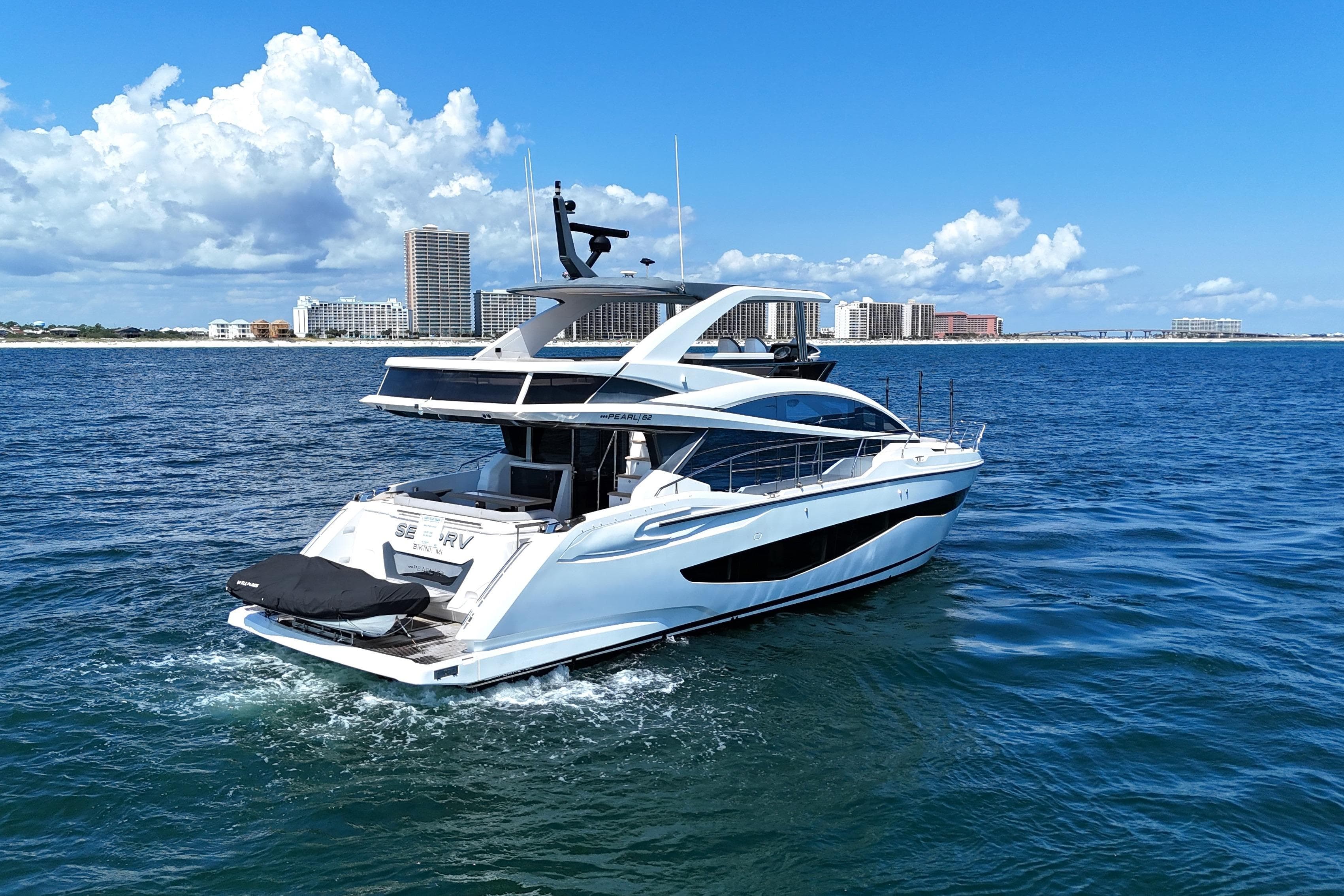 Luxurious 2022 Pearl 62 yacht cruising on a sunny day near coastal cityscape.