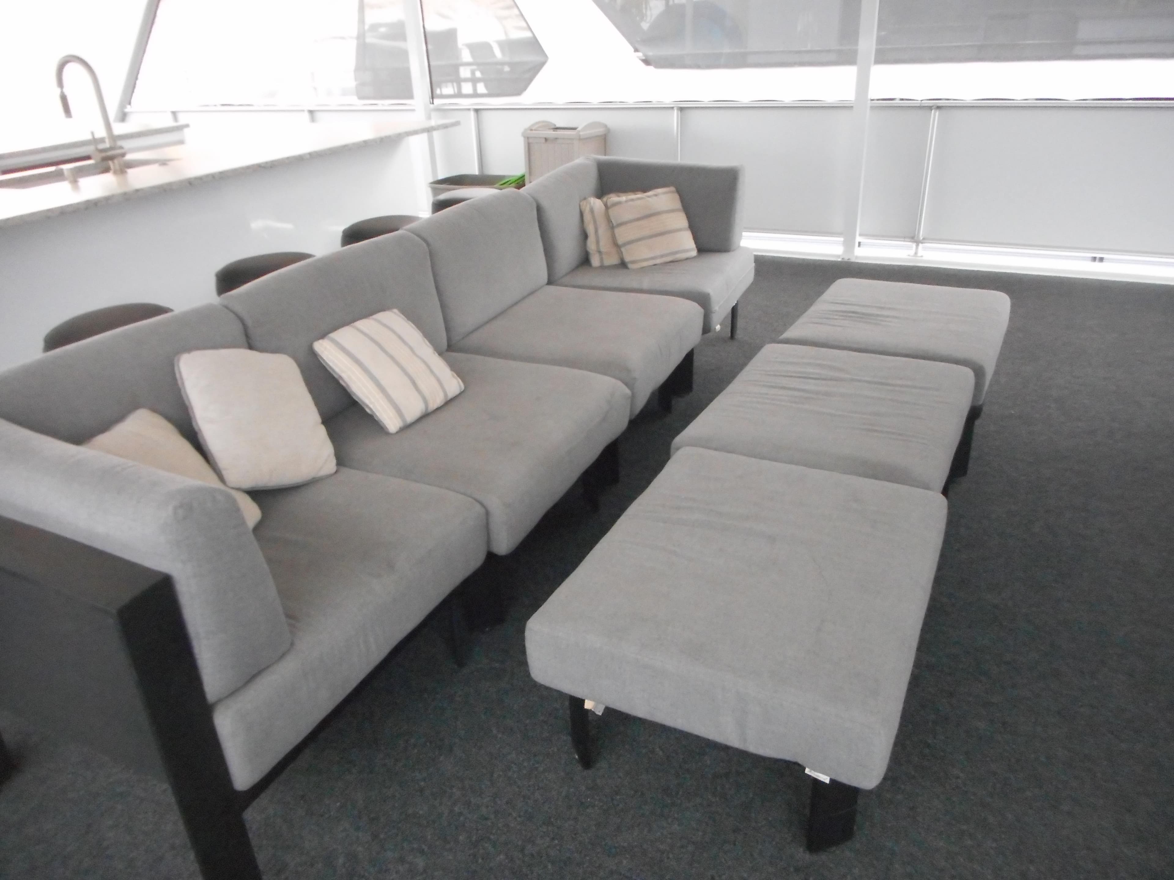 Gray seating area on Adonia Liquidity Trip 5 yacht, 2017 model, with cushions and stools.