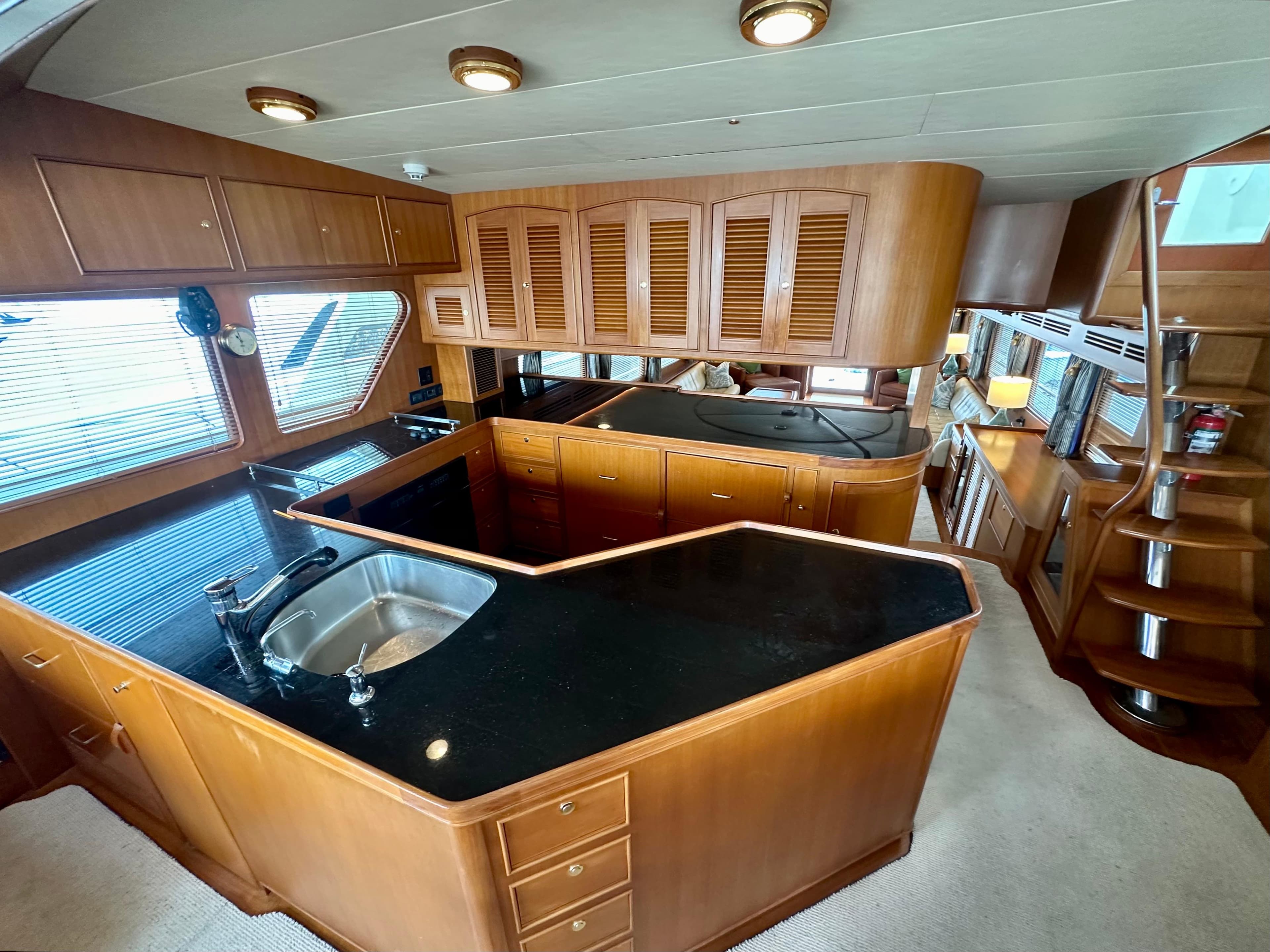 Luxurious kitchen interior of 2005 Marlow Explorer 78 yacht with wooden cabinetry and black countertops.