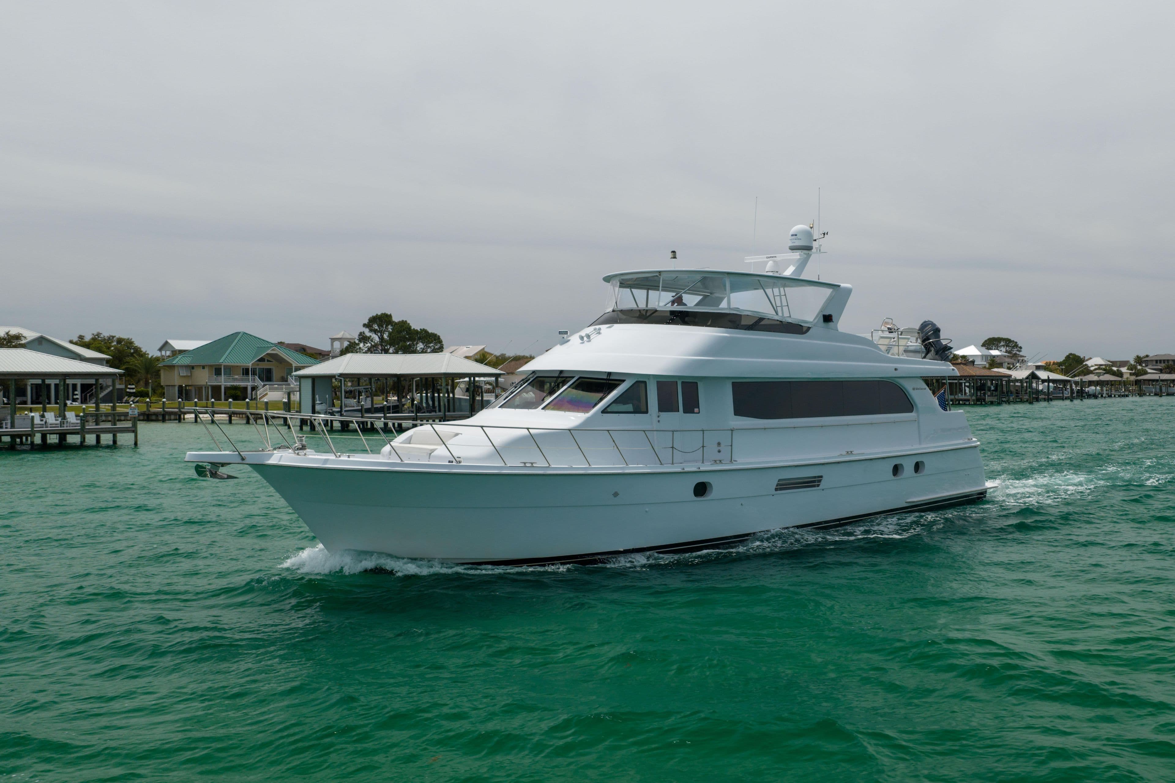 2004 Hatteras 75 Sport Deck Motor Yacht cruising on turquoise waters near docks.
