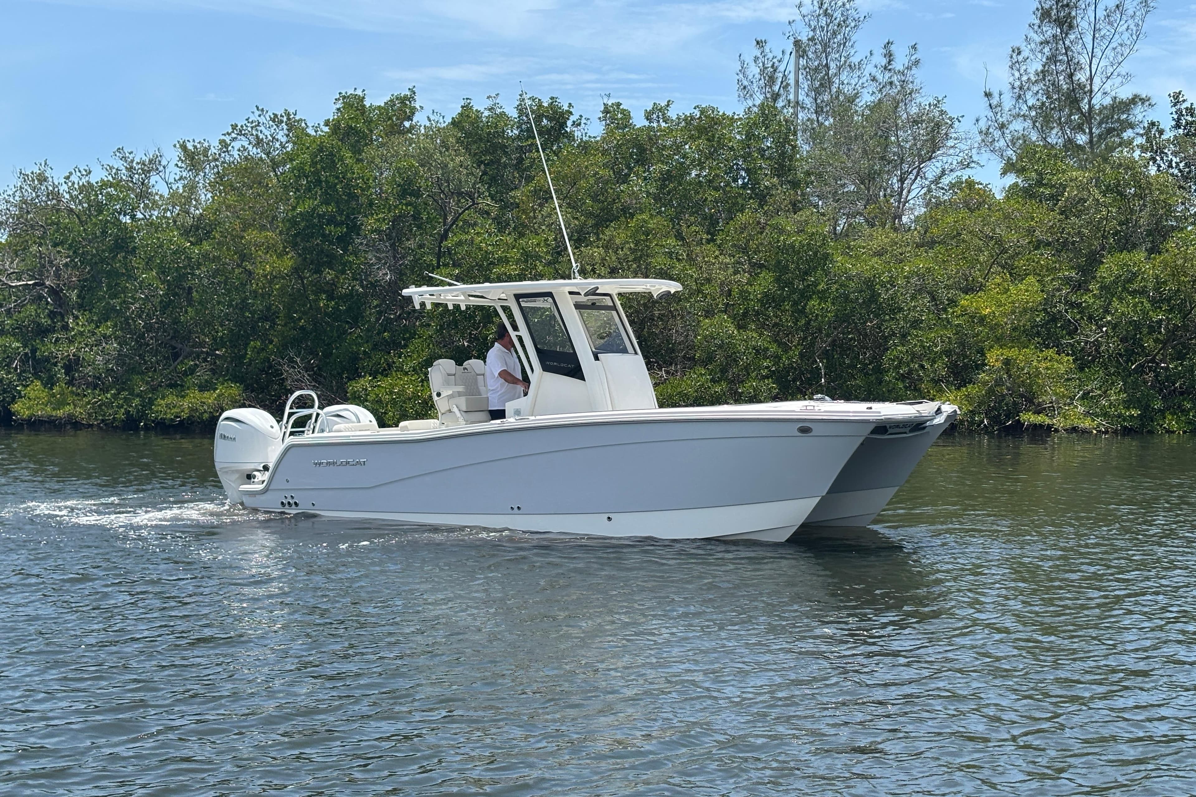2026 World Cat 265 CC-X boat cruising on a calm river with lush greenery.